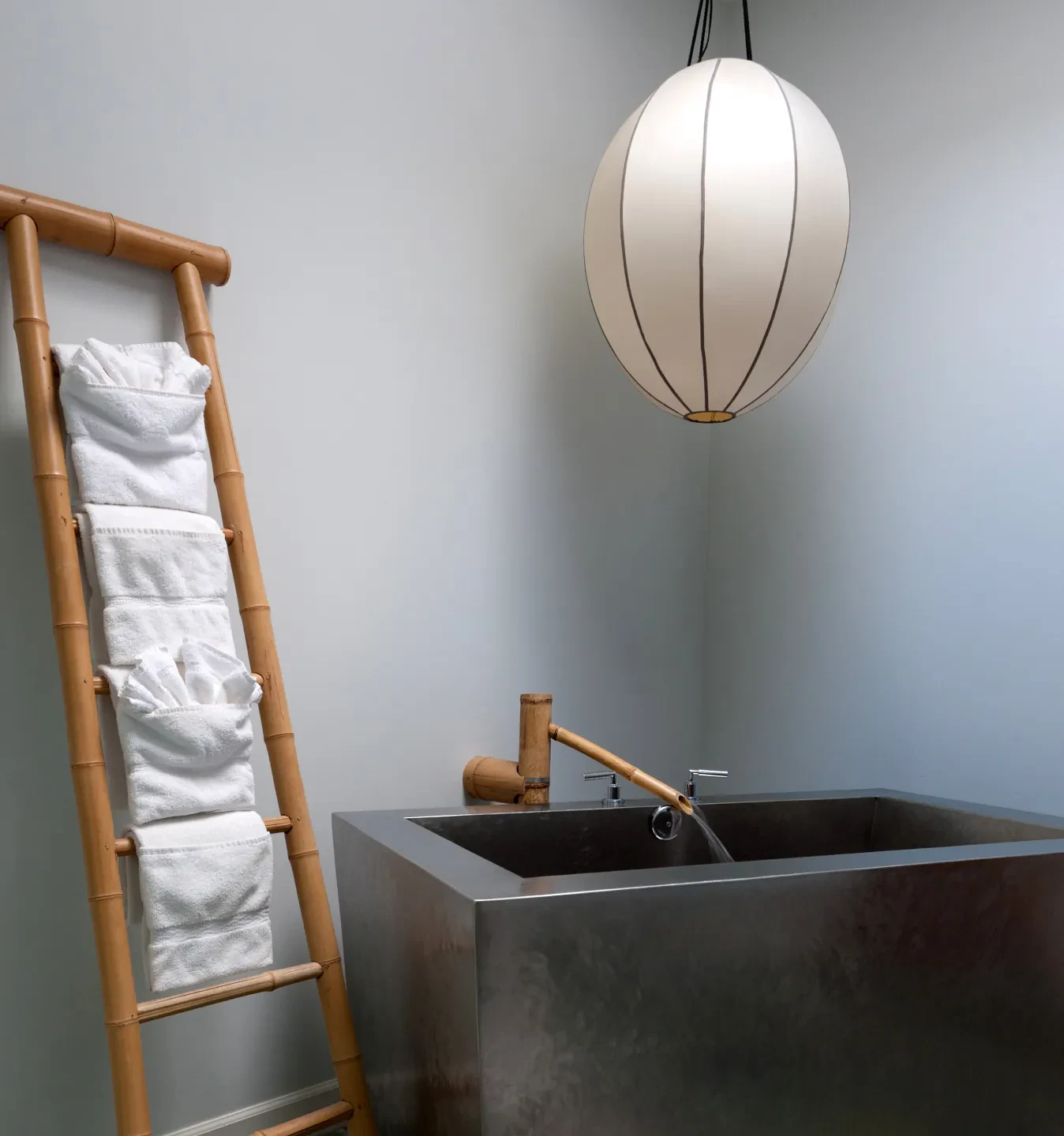 Bamboo towel ladder beside a stone soaking tub and pendant lamp