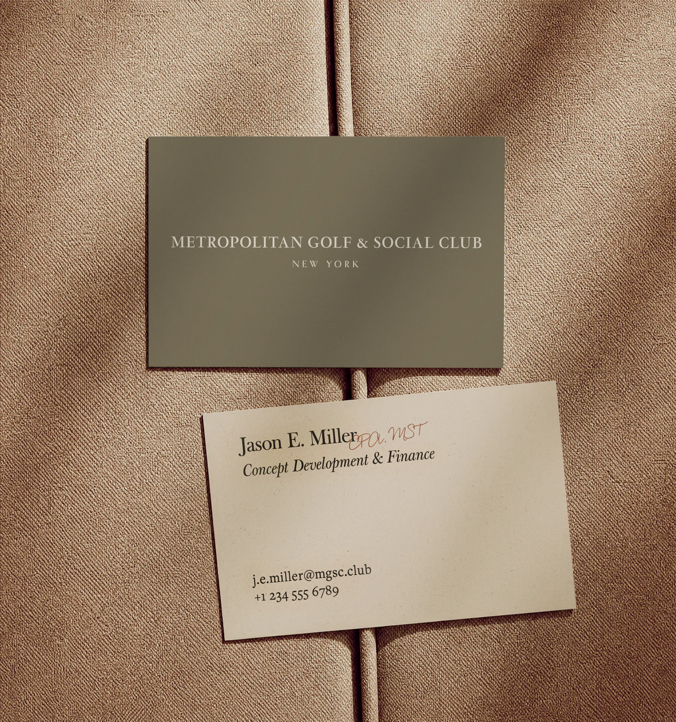 2 business cards laying on a tan fabric cushion, one side depicting the front with the MGSC logo and the other showing the back of the card which has employee information