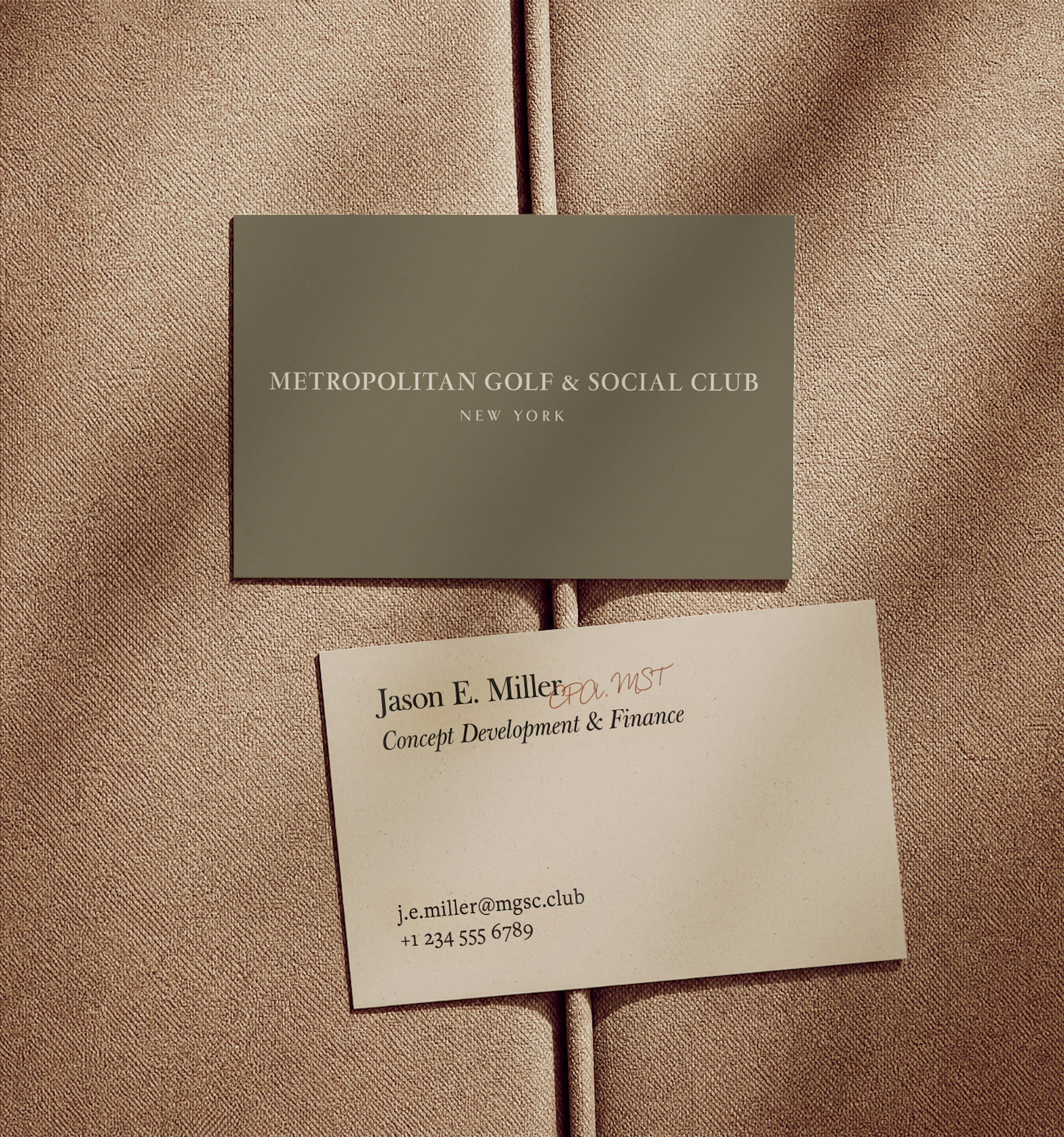 2 business cards laying on a tan fabric cushion, one side depicting the front with the MGSC logo and the other showing the back of the card which has employee information