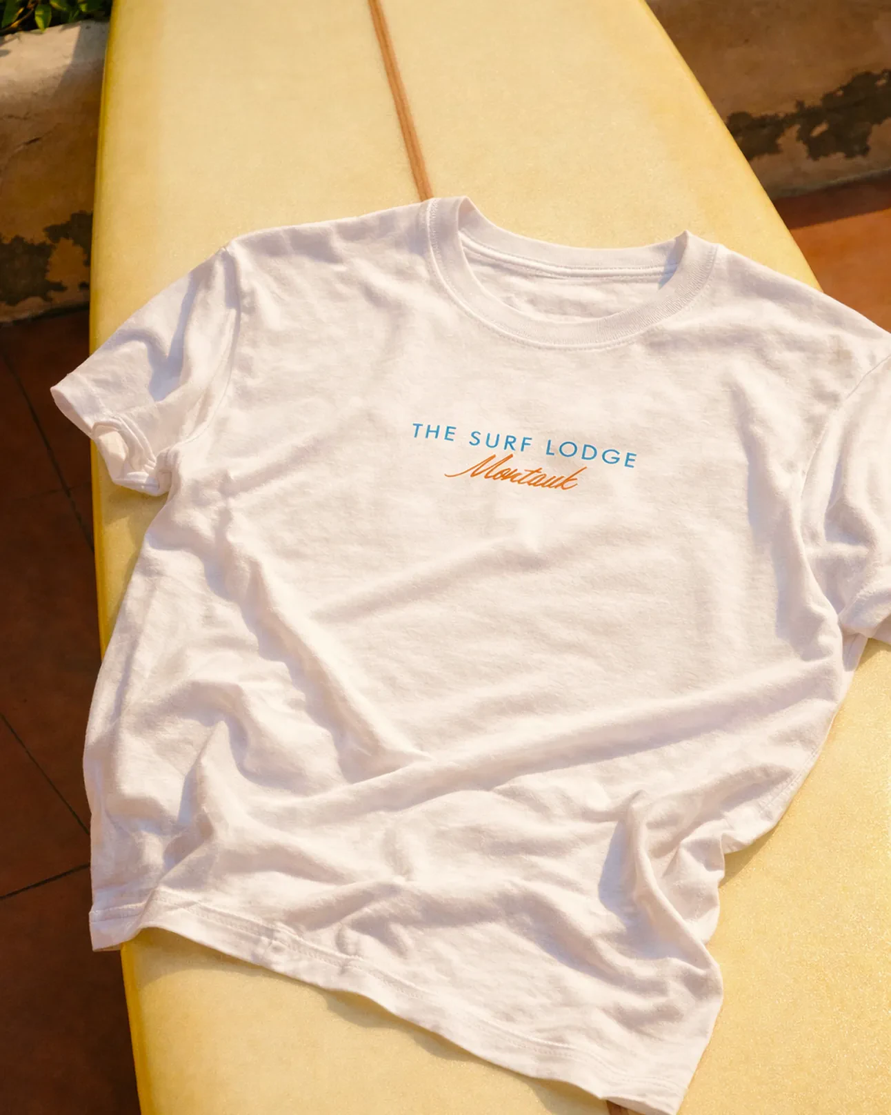The Surf Lodge Montauk t-shirt laid on a surfboard