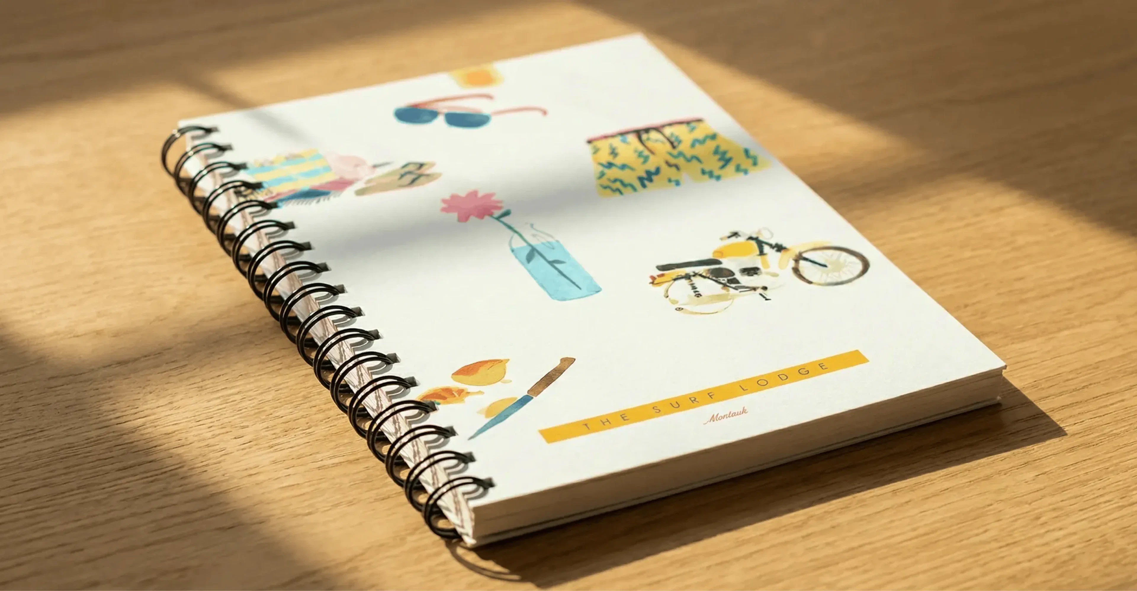 Spiral notebook with illustrated icons on a wood table in sunlight