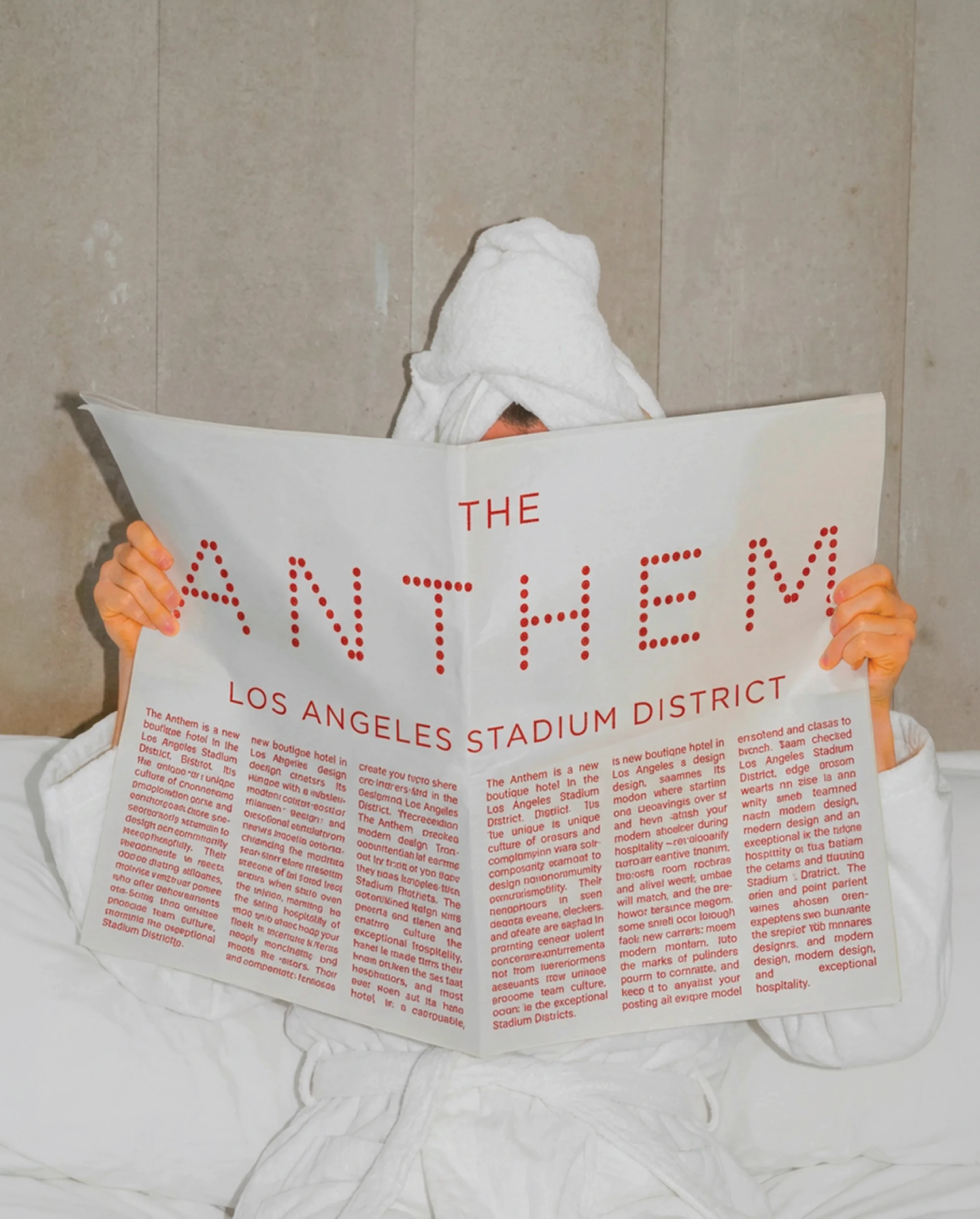 Person under towel reading Anthem hotel newspaper mockup in bed