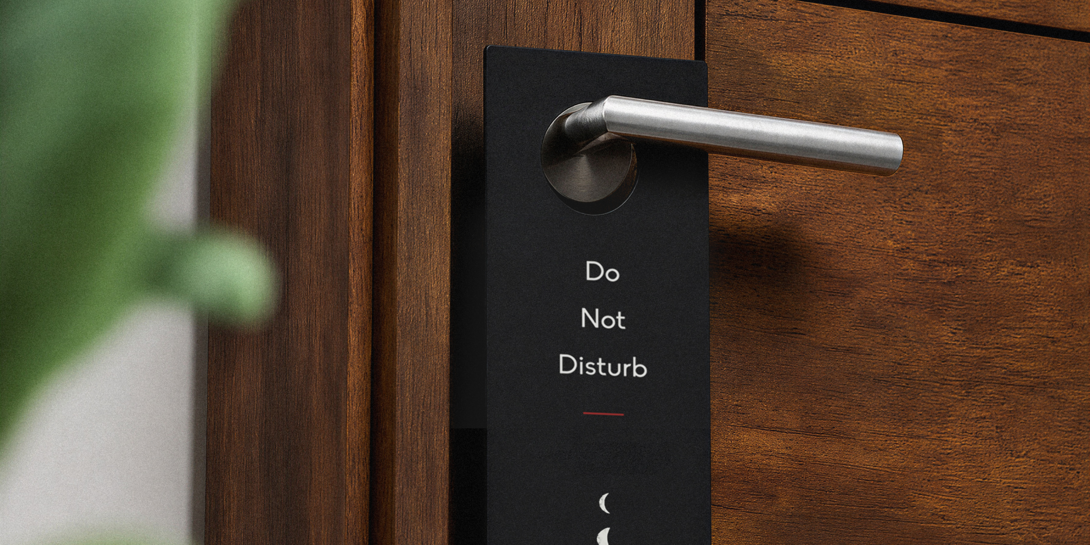 Black branded door hanger saying "Do not disturb" hanging on a silver door handle attached to a dark wood modern door