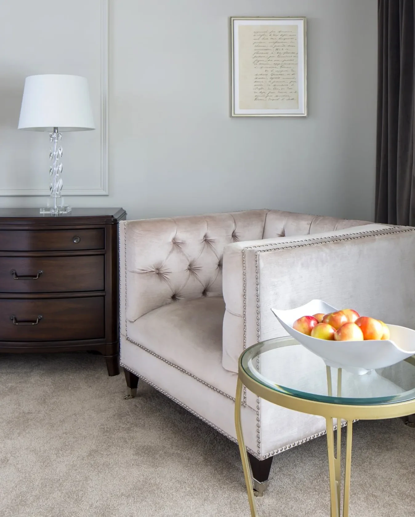 Living room corner with tufted armchair, dark wood nightstand and glass side table