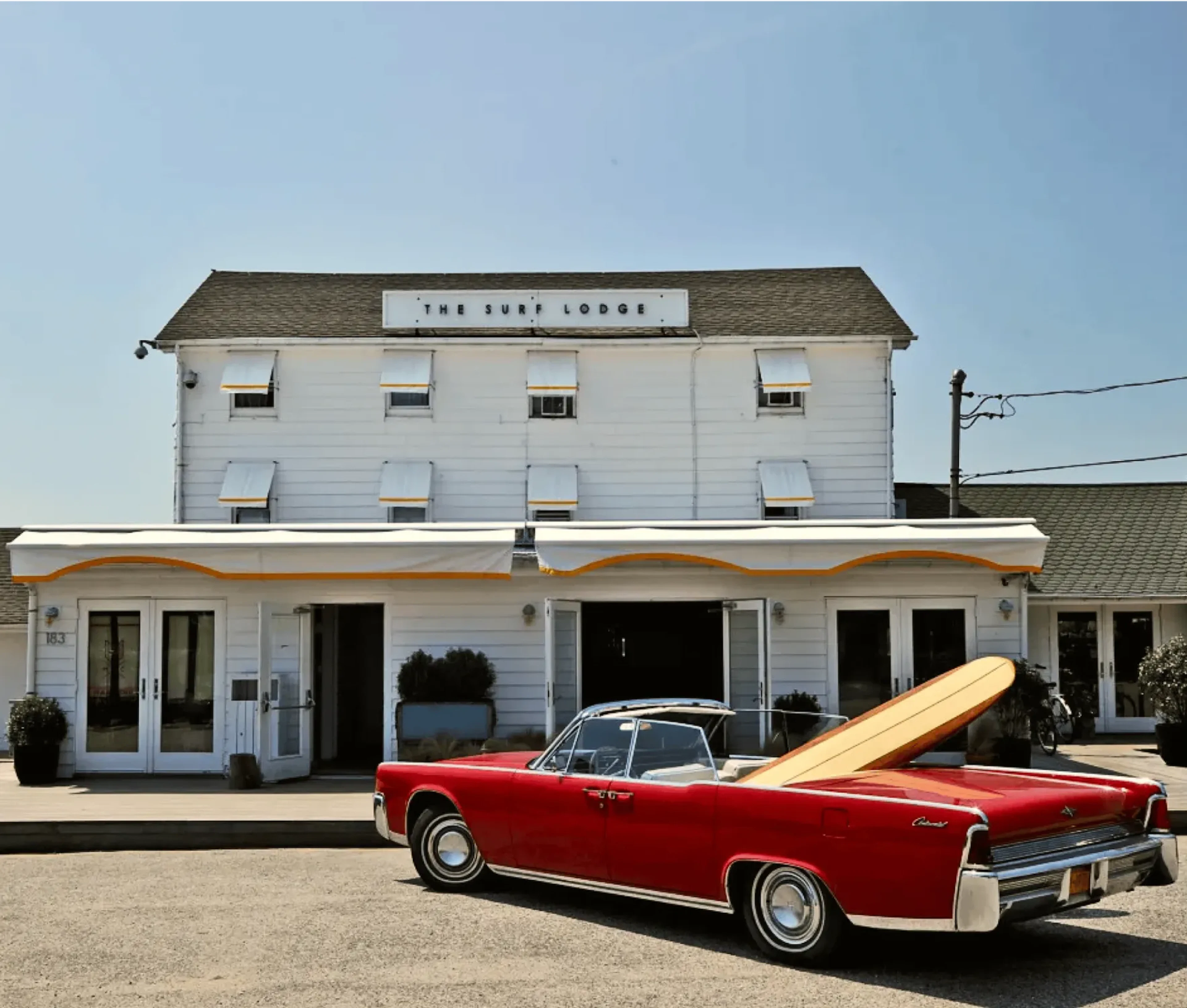 Image of the Surf Lodge building with a beautiful red retro convertible with a surfboard in the back seat in front of it.