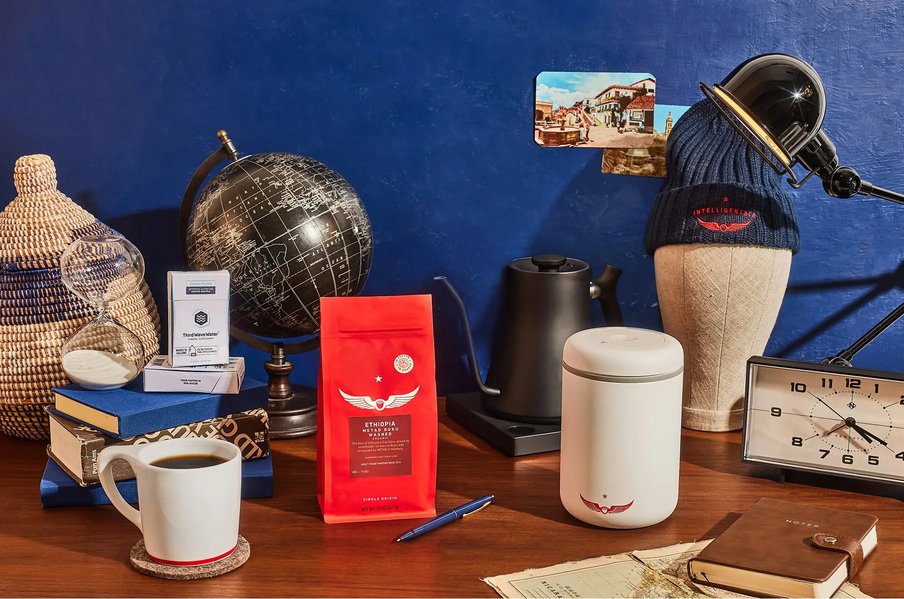 Coffee bag, mug and desk accessories on a wood desk against a blue wall