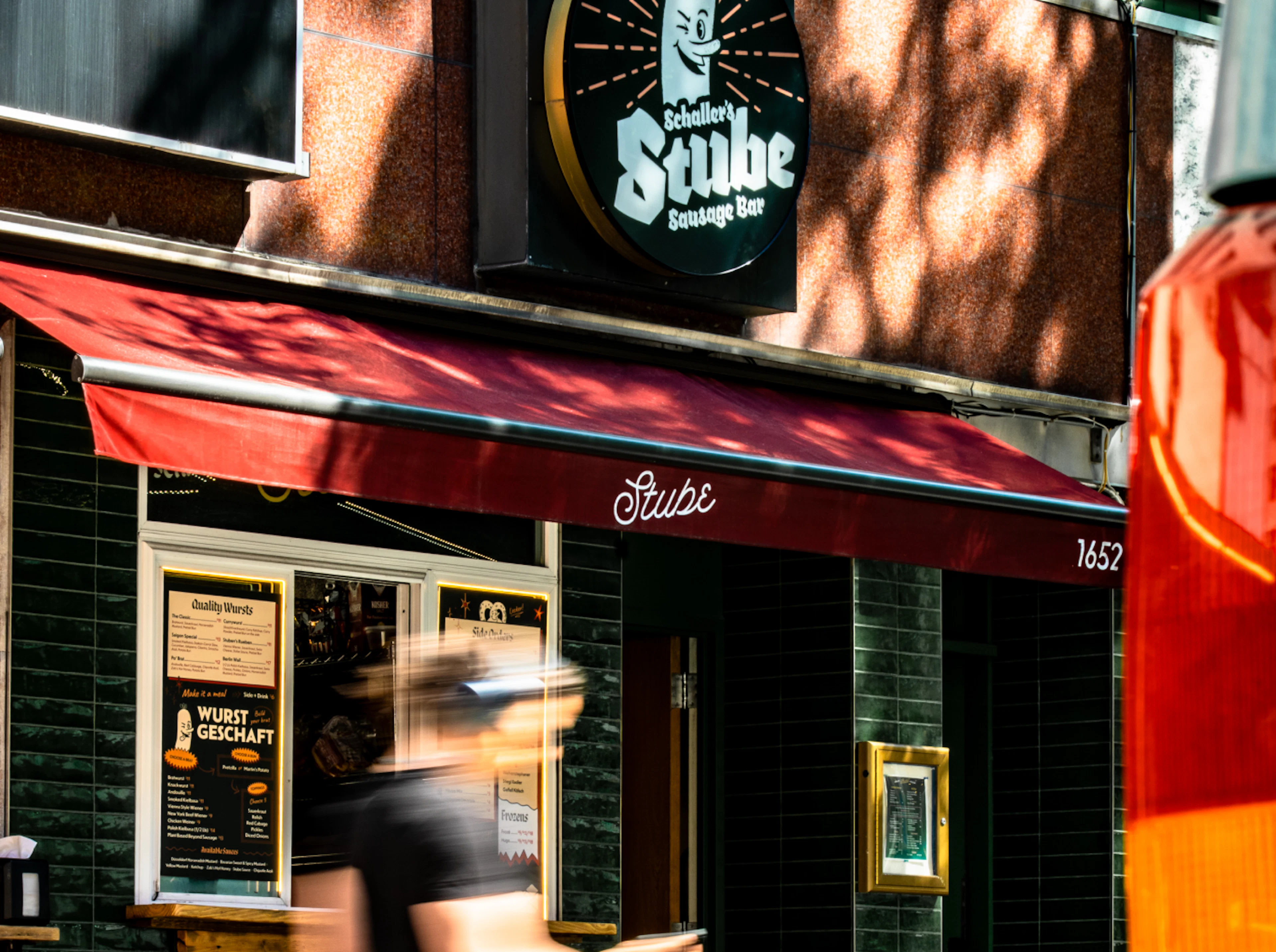 Man walking down the street in front of the Stube, he's motion blurred and it's a sunny day in NYC