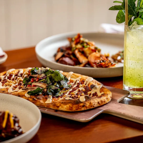 Flatbreads, cocktails and appetizers on a wood table in a bright restaurant setting