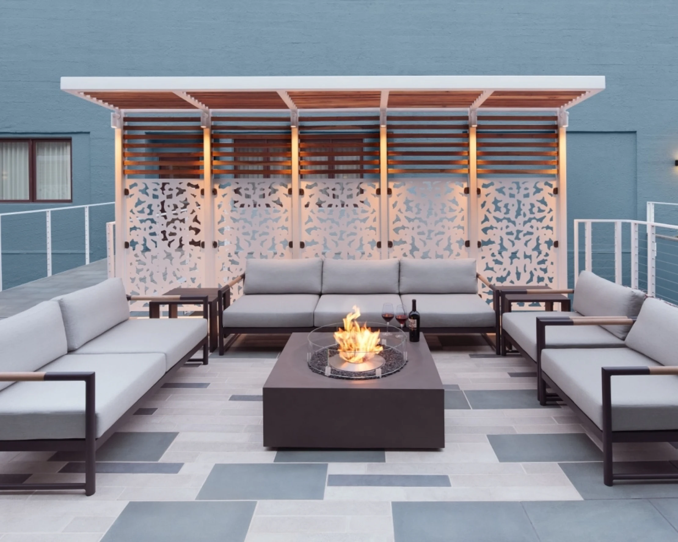 A stylish hotel exterior patio with modern fabric couches, a square coffee table fireplace and tile flooring