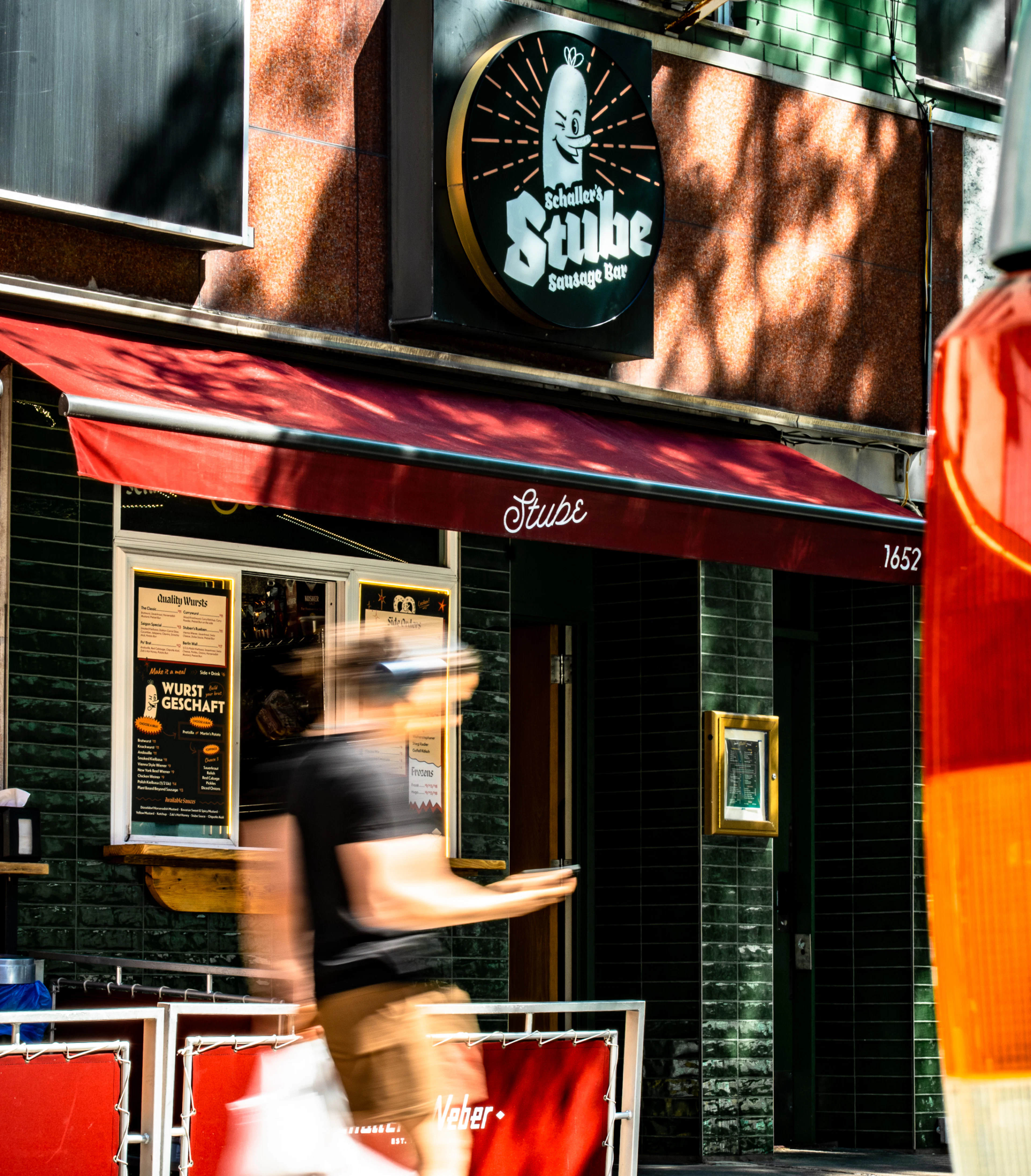 Man walking down the street in front of the Stube, he's motion blurred and it's a sunny day in NYC