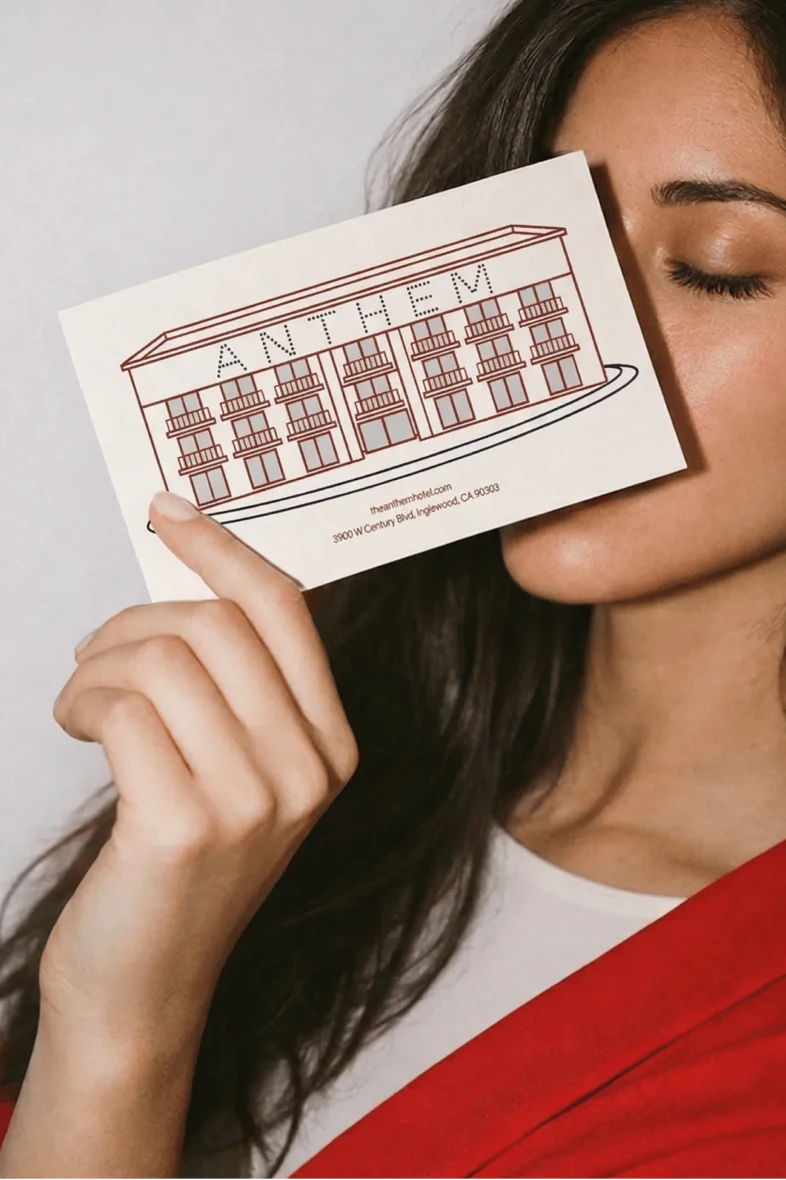 A woman holding a postcard up to her face, eyes closed, the postcard has an illustration of the Anthem hotel on the front