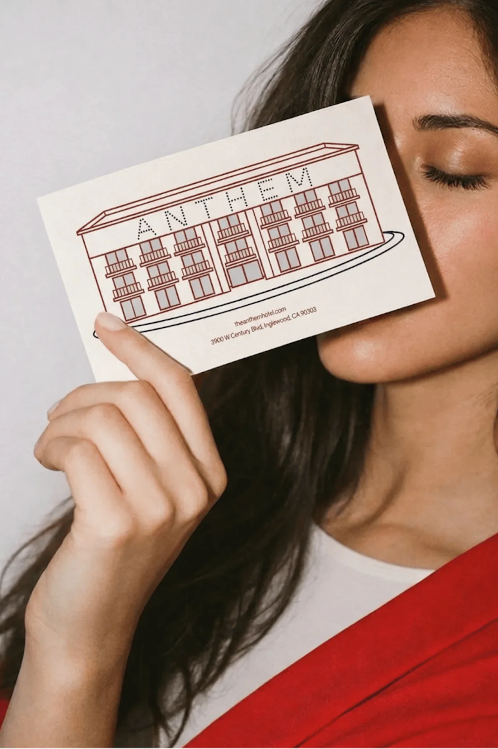 A woman holding a postcard up to her face, eyes closed, the postcard has an illustration of the Anthem hotel on the front