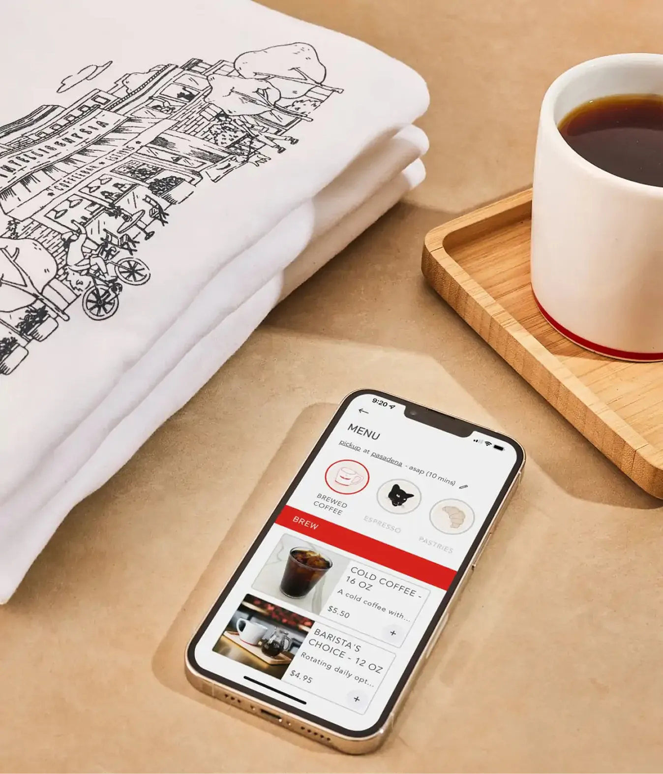 Folded t-shirt, coffee mug and phone showing a menu app