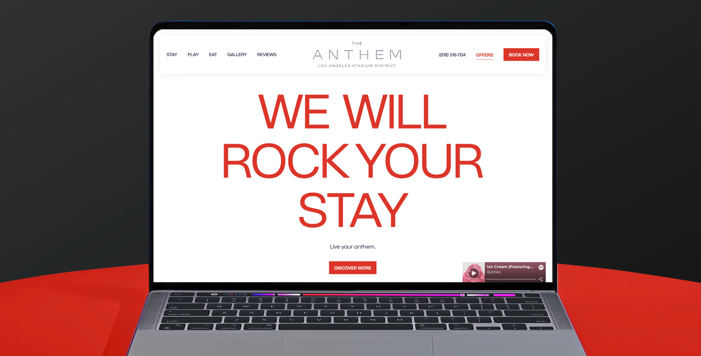 An open laptop sitting on a red table with a black background, the screen showcases the home page of the Anthem Hotel