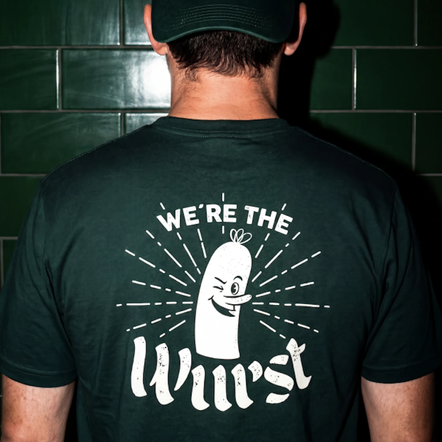 Back of a person wearing a Stube Sausage Bar cap and We're the Wurst t-shirt