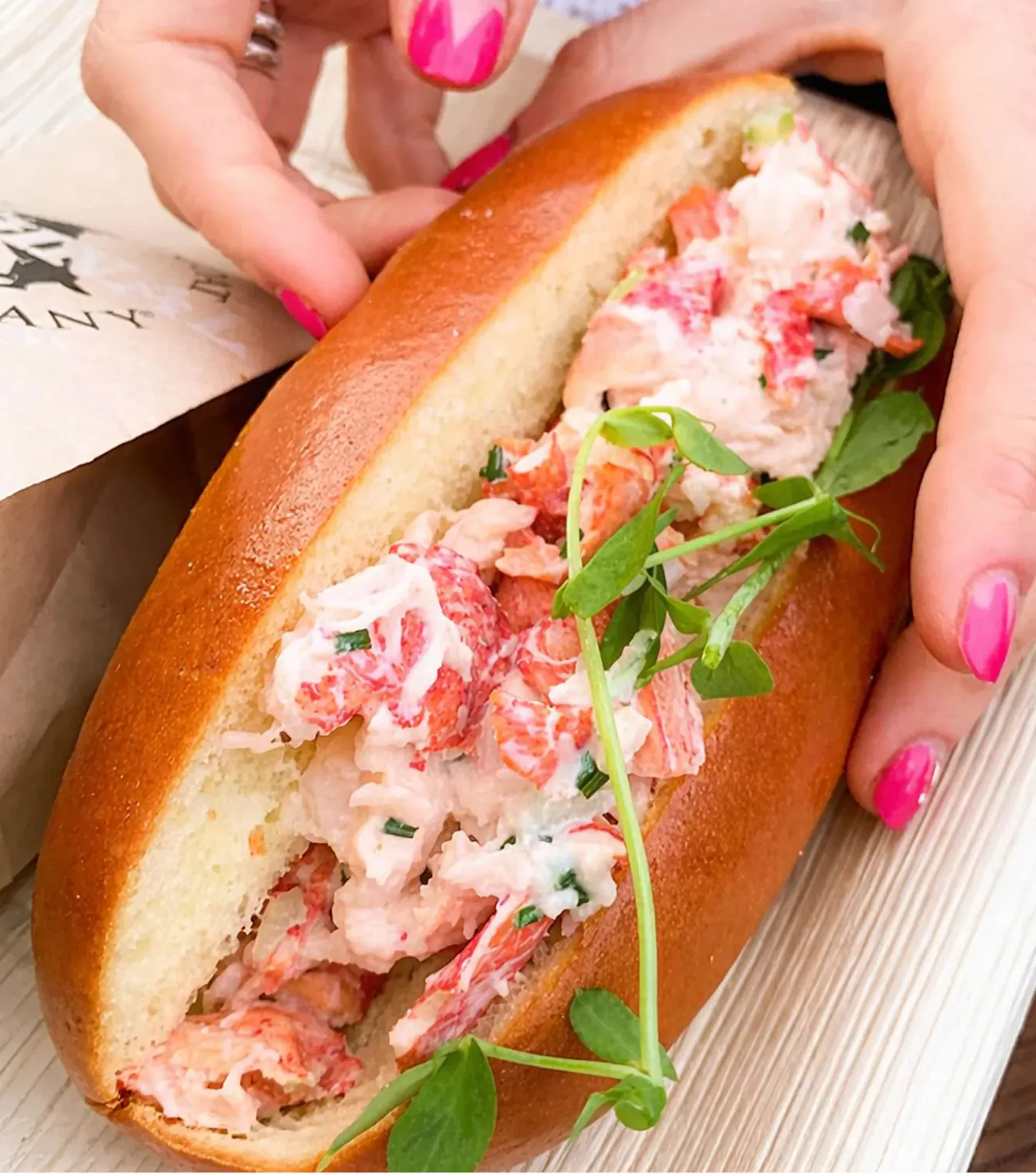 Hands holding a lobster roll with pea shoot garnish