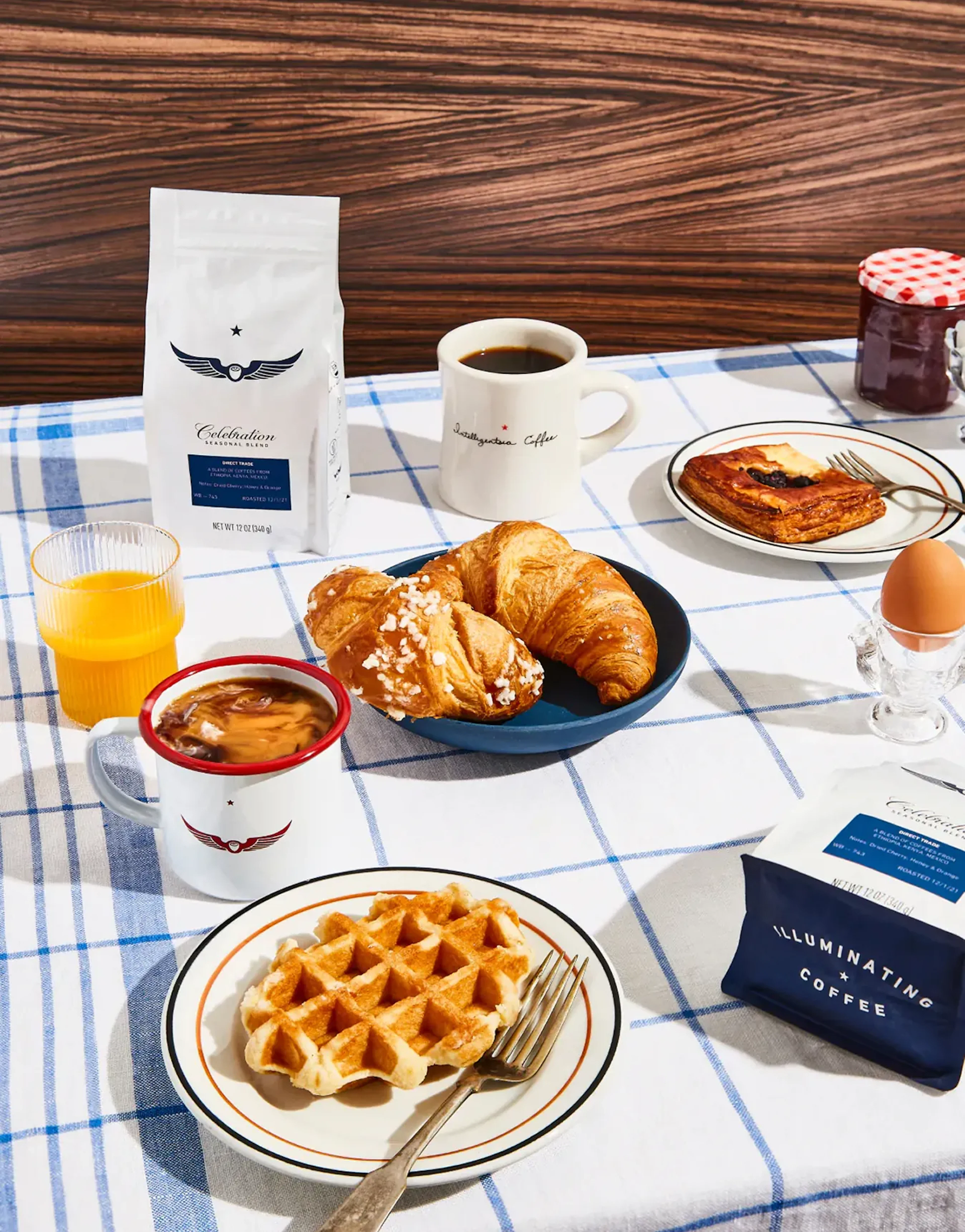 Breakfast spread of coffee bags, croissants, waffle, and orange juice on a checkered tablecloth