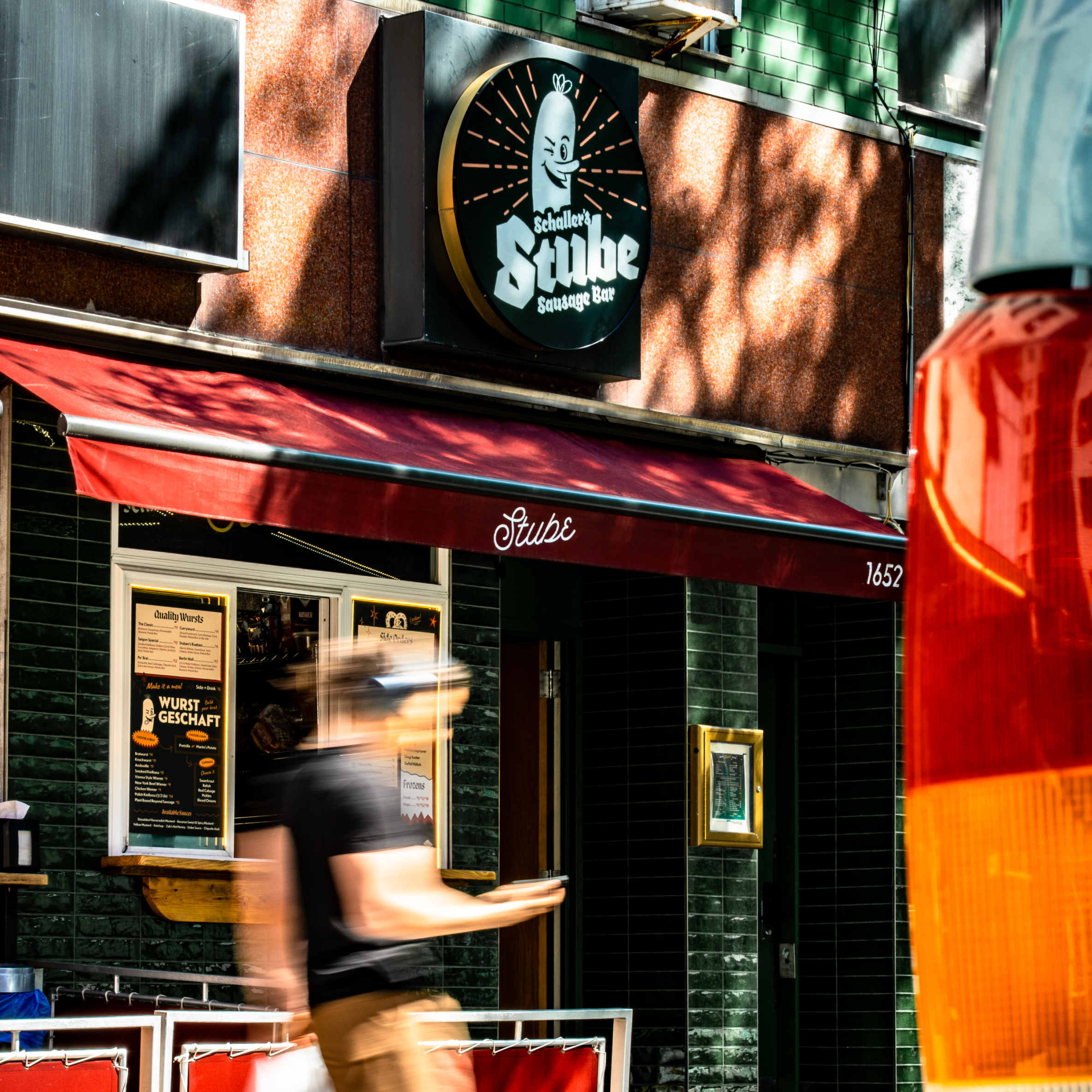 A person walking in front of the Stube restaurant outside in NYC on a bright sunny day