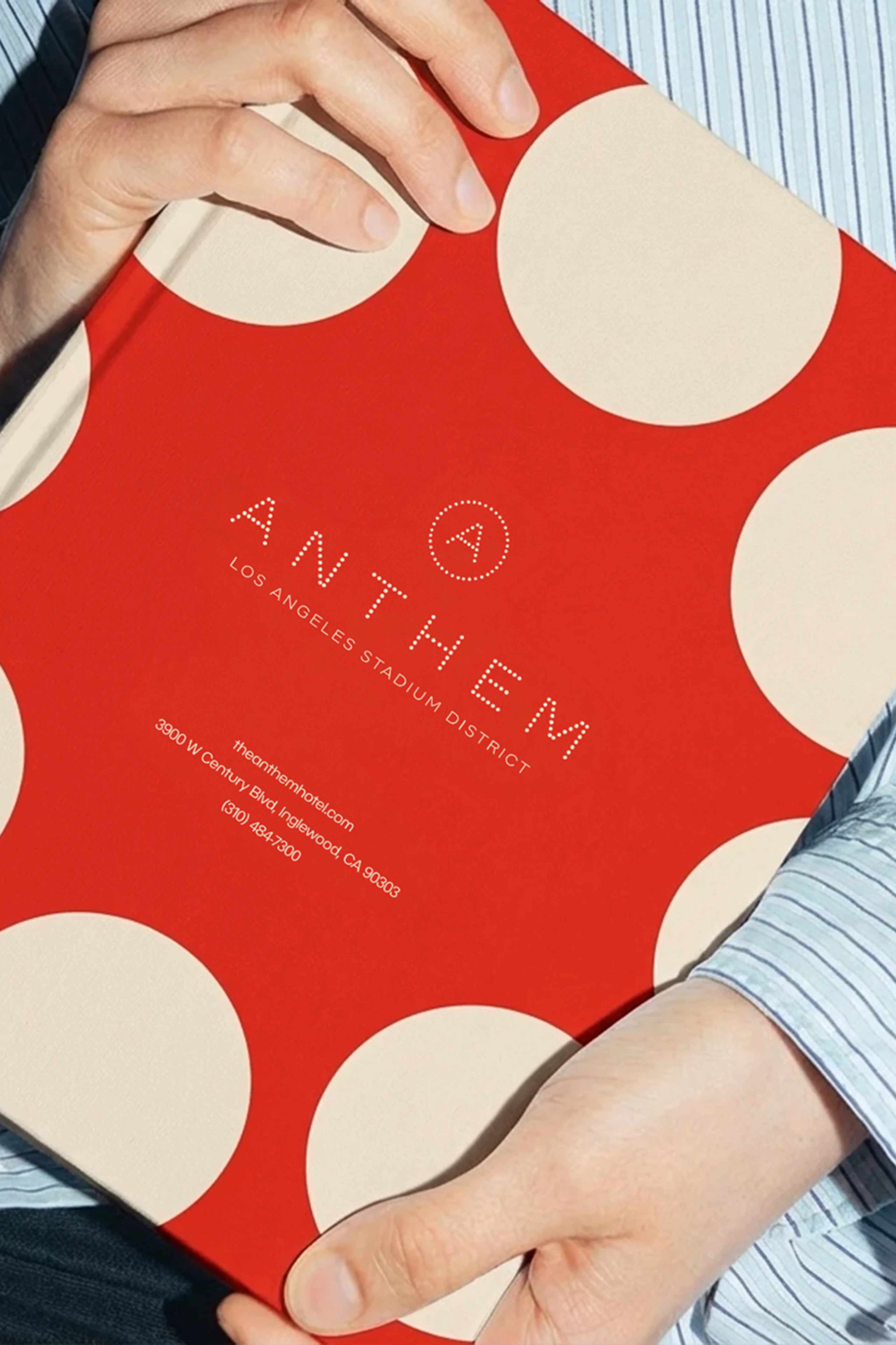 Red polka dot Anthem booklet held by a person in a striped shirt