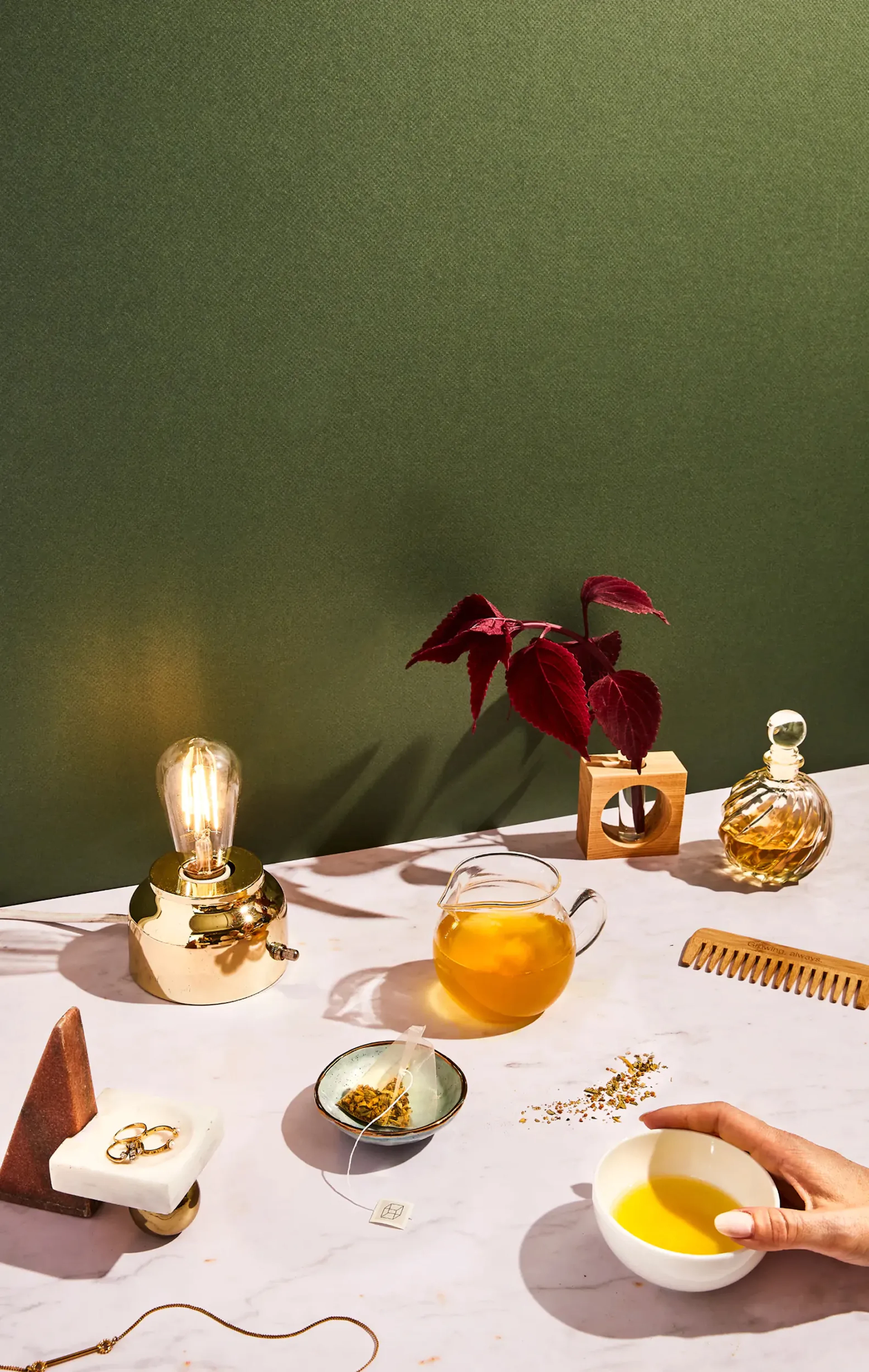 Overhead tabletop styling with a brass lamp, teapot, small bowls, comb, and jewelry on marble
