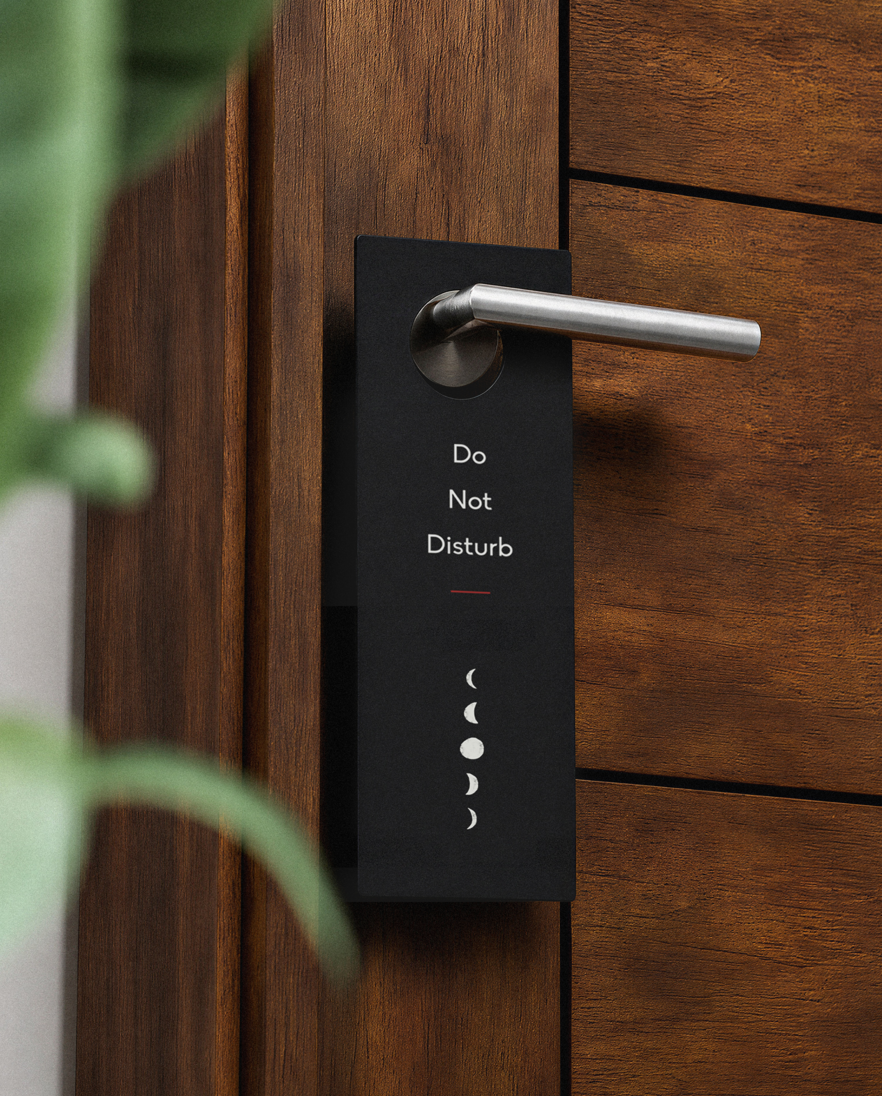 Black branded door hanger saying "Do not disturb" hanging on a silver door handle attached to a dark wood modern door