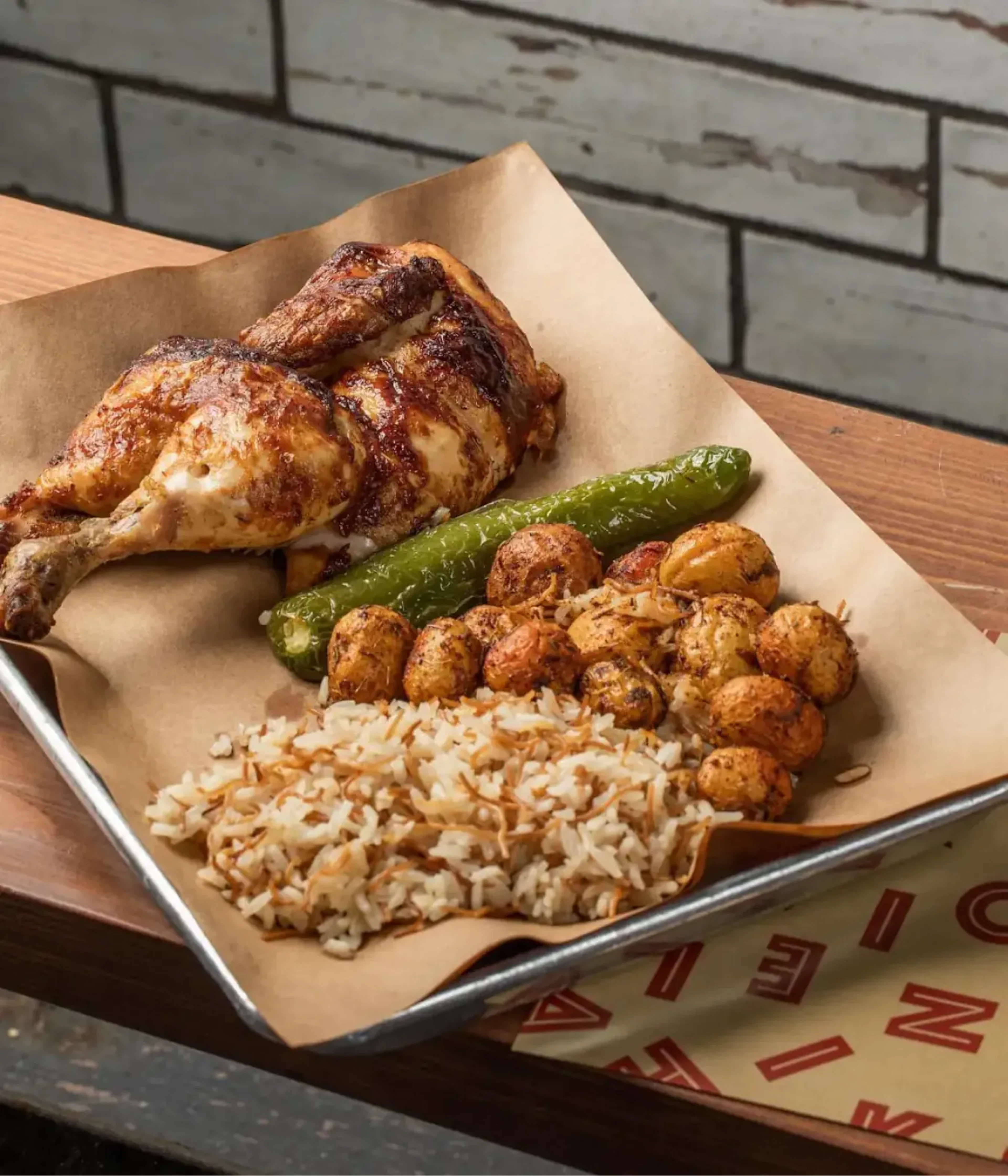 Tray of roast chicken, grilled pepper, and rice on a wooden table