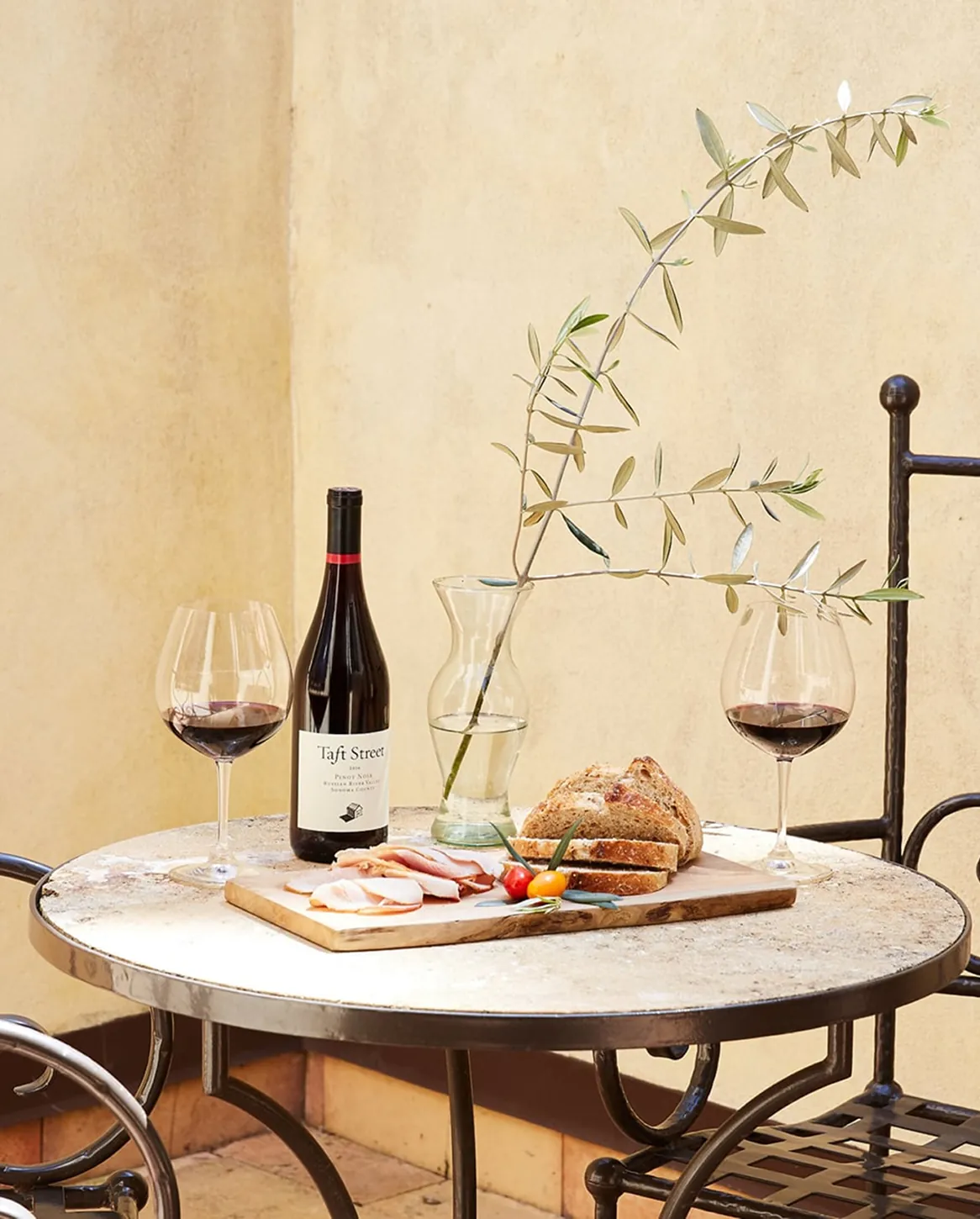 Wine bottle, glasses and bread board on outdoor table