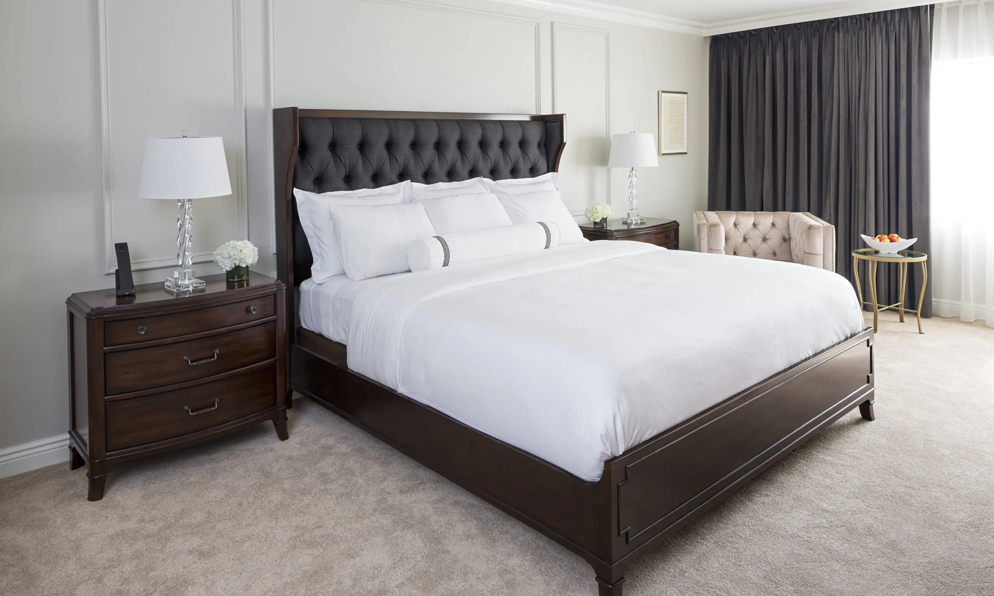 Bedroom with dark tufted headboard, white bedding and brown wood nightstands