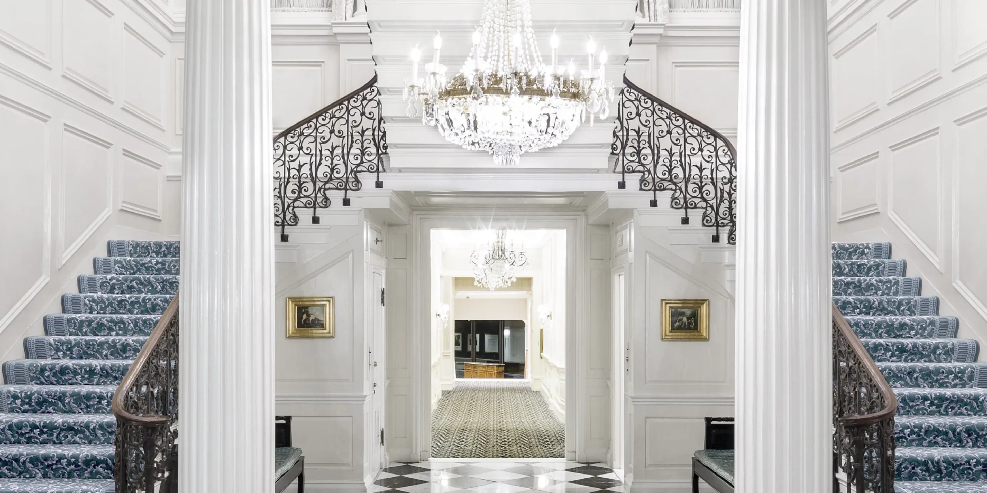 Grand entry hall with crystal chandelier, blue striped staircase and checkerboard floor