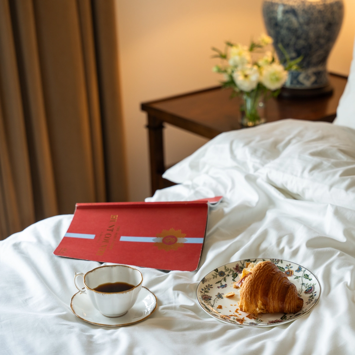 Coffee, croissant and red book on hotel bed