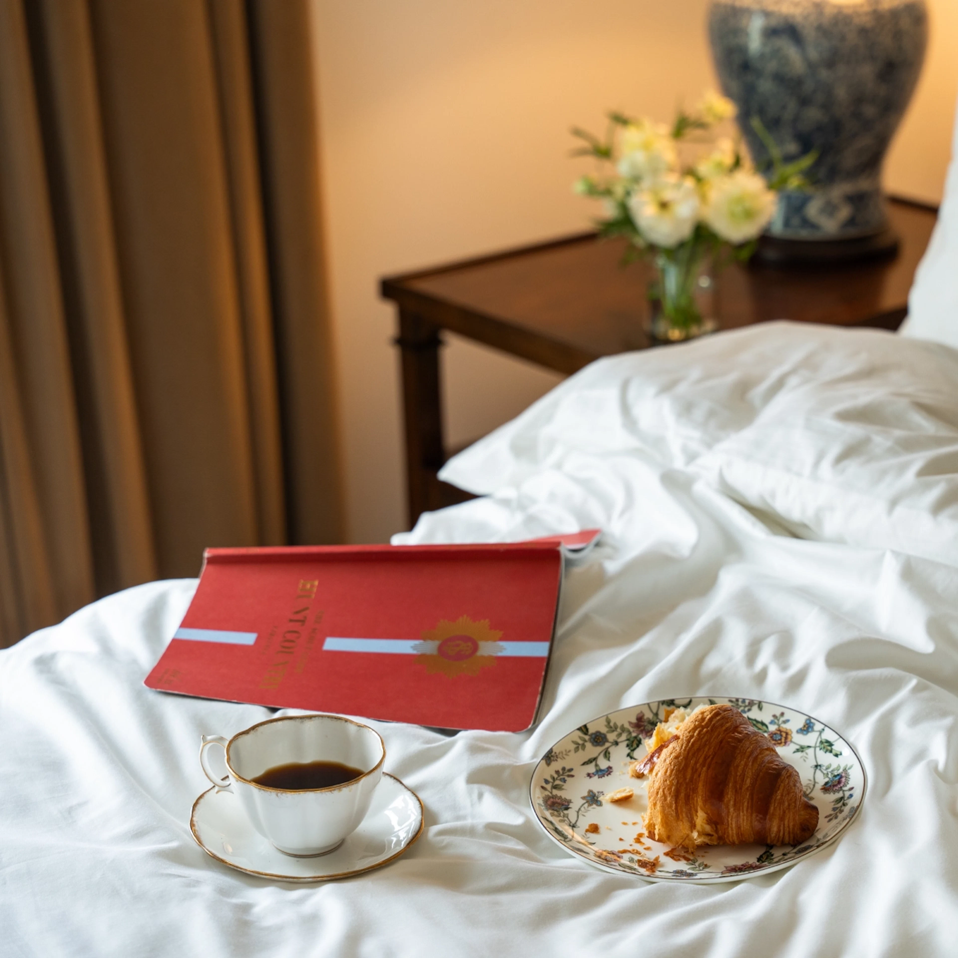 Coffee, croissant and red book on hotel bed