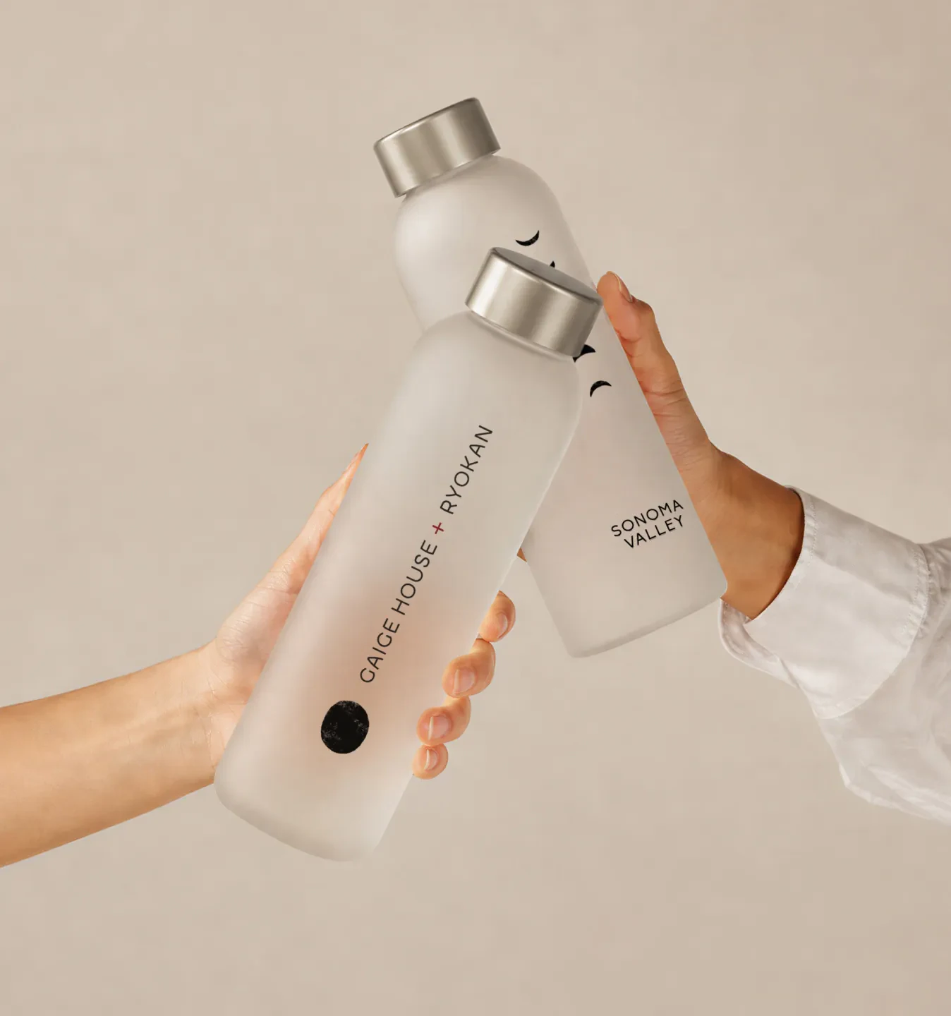 Two hands holding frosted Gaige House and Ryokan water bottles