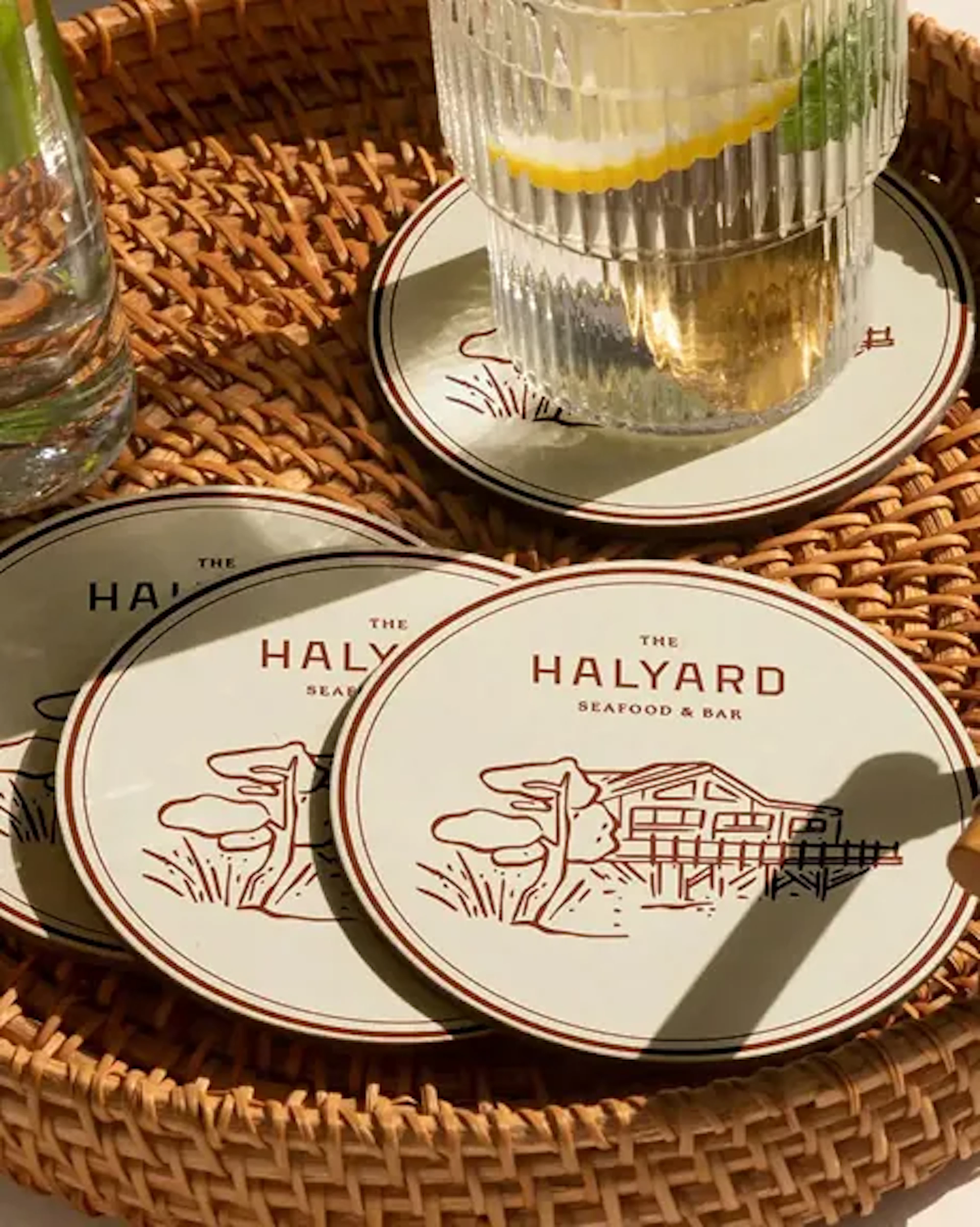 The Halyard branded coasters on a woven tray with a drink