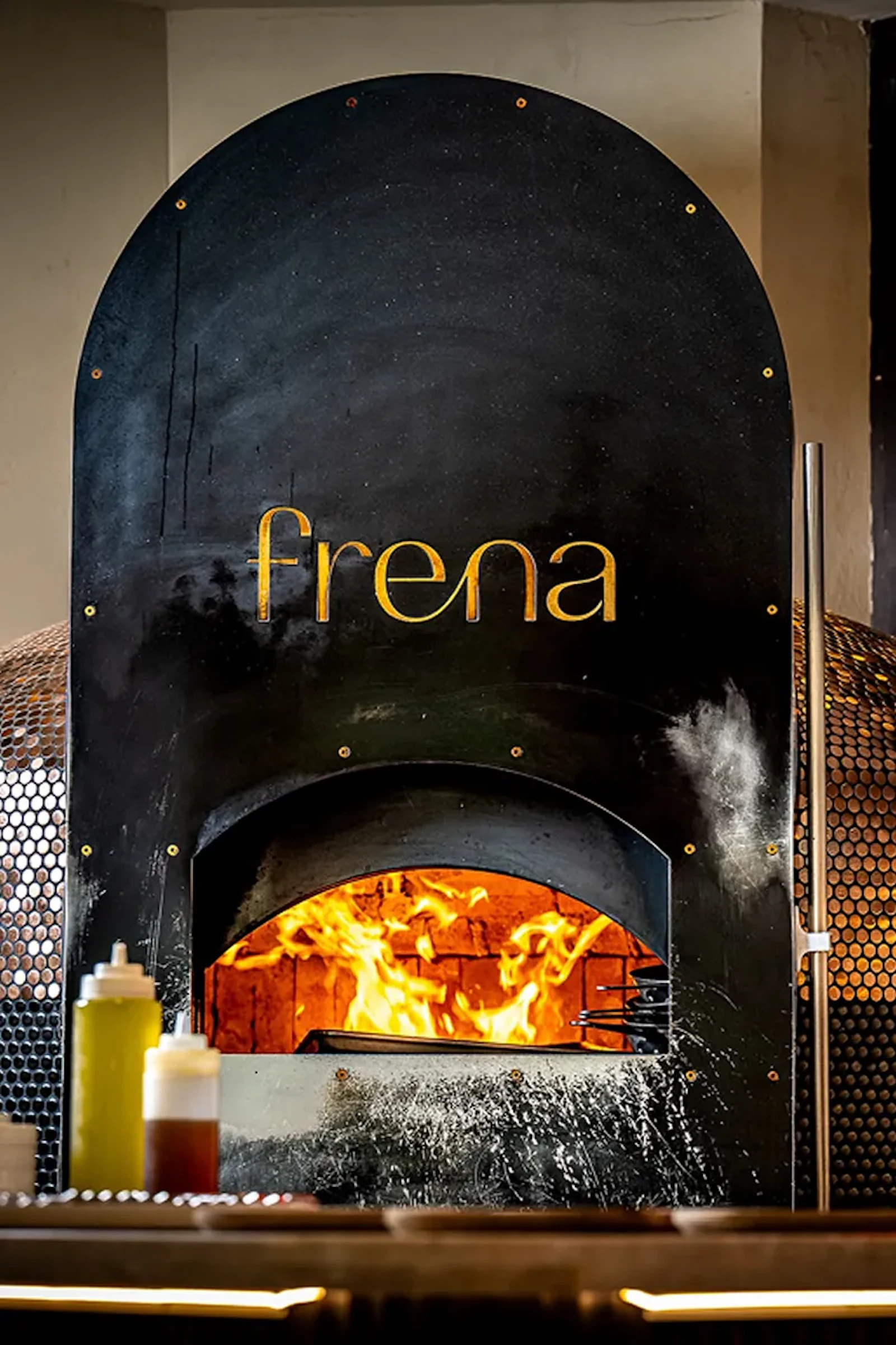 Frena wordmark on a black wood-fired oven with flames inside