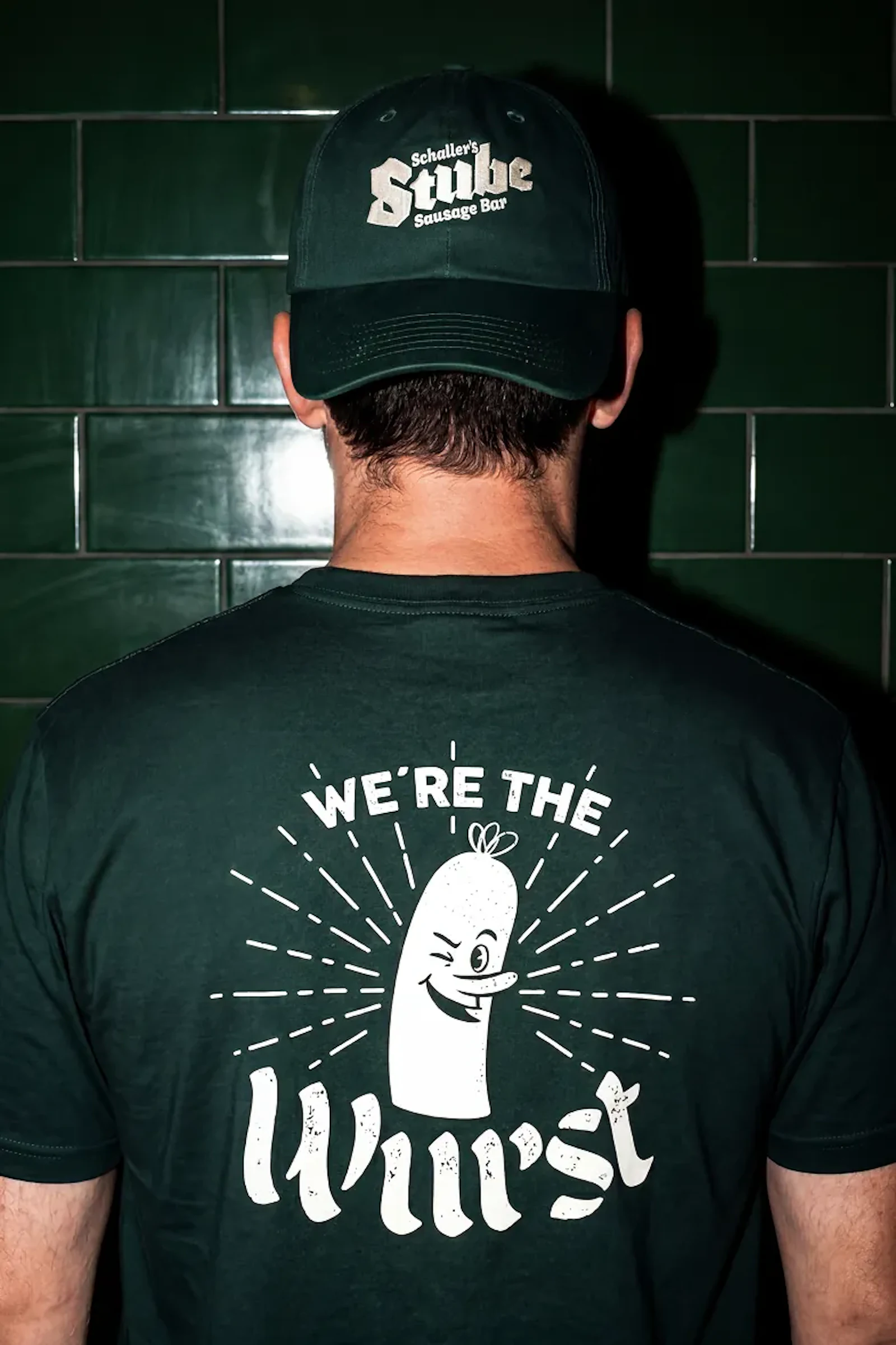 Back of a person wearing a Stube Sausage Bar cap and We're the Wurst t-shirt