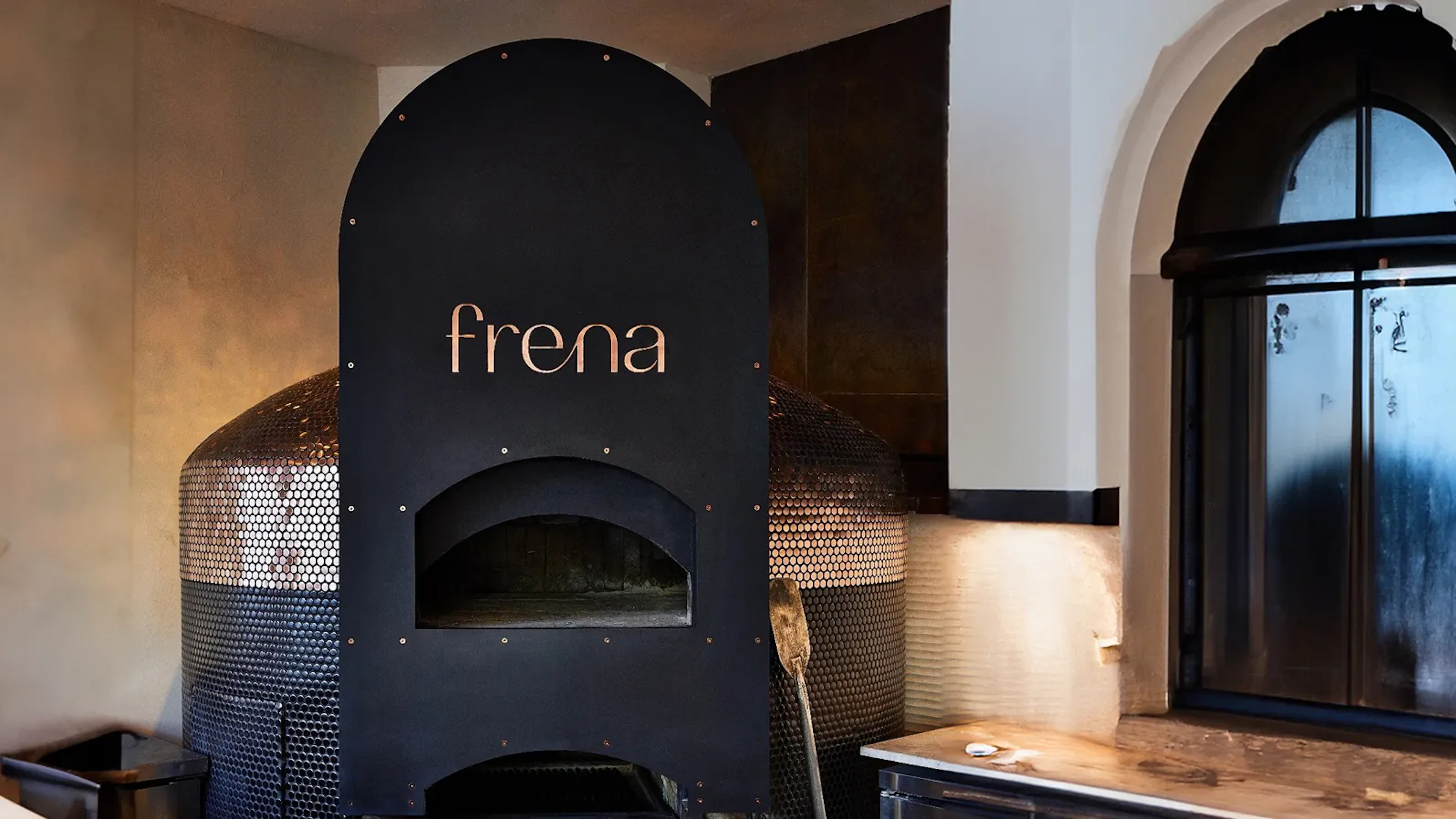 Frena wordmark on a black wood-fired oven in a restaurant