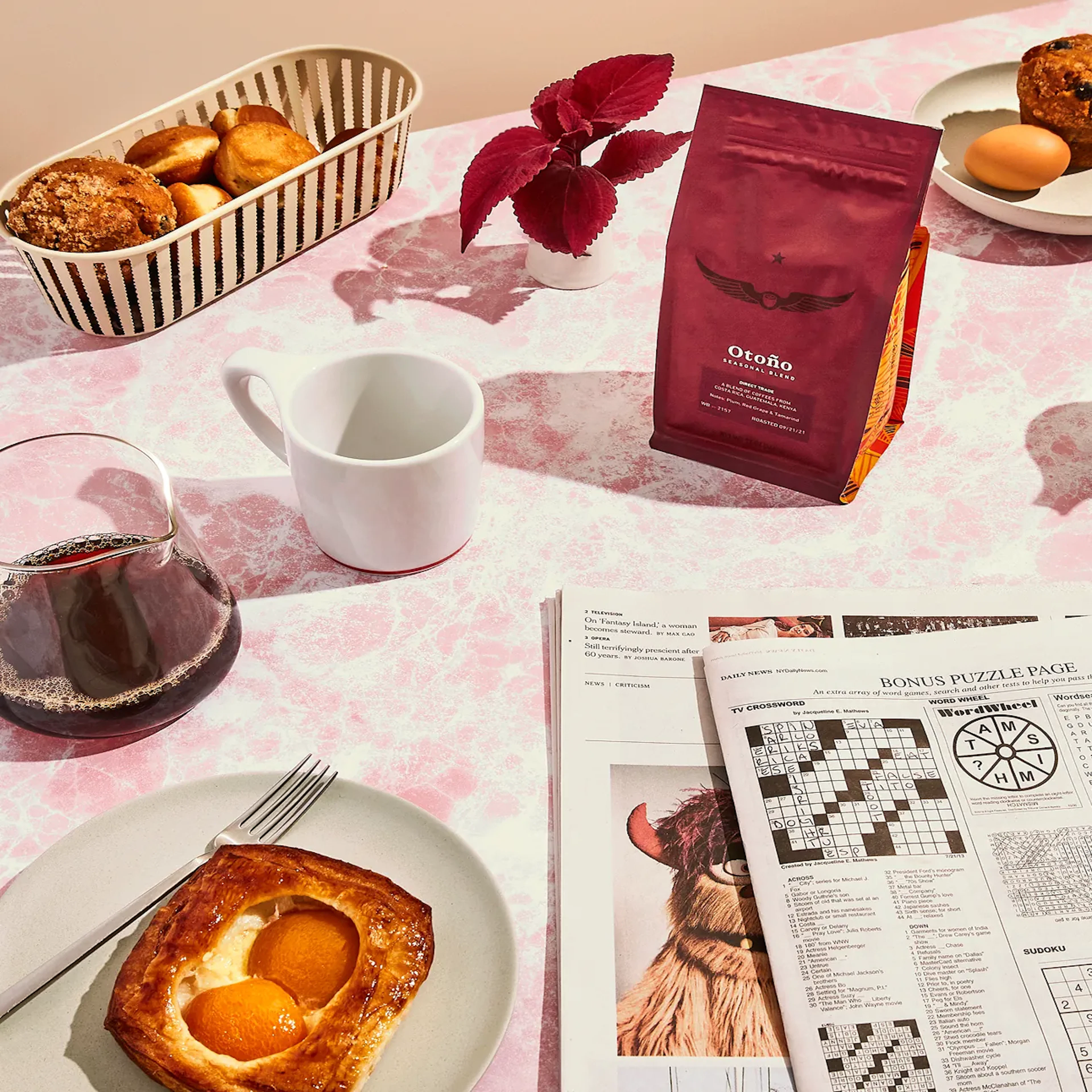 Breakfast table with pastries, coffee, wine, and a newspaper puzzle page