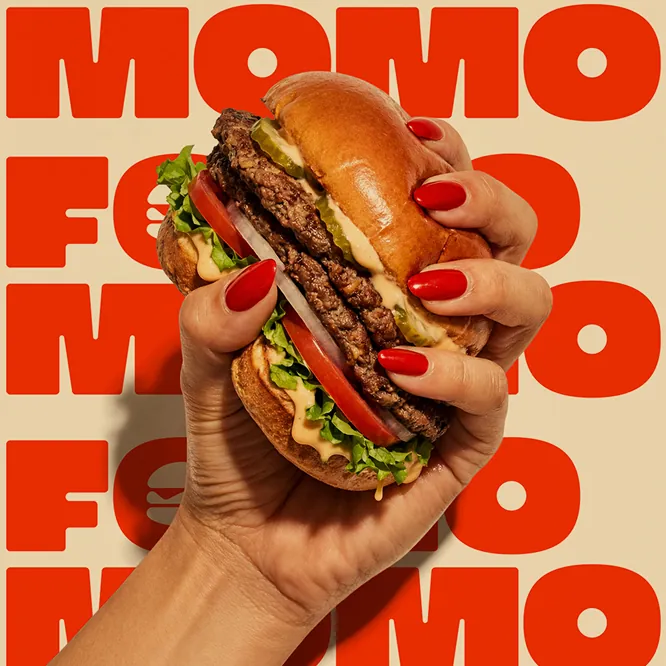 Hand with red fingernails holding a burger