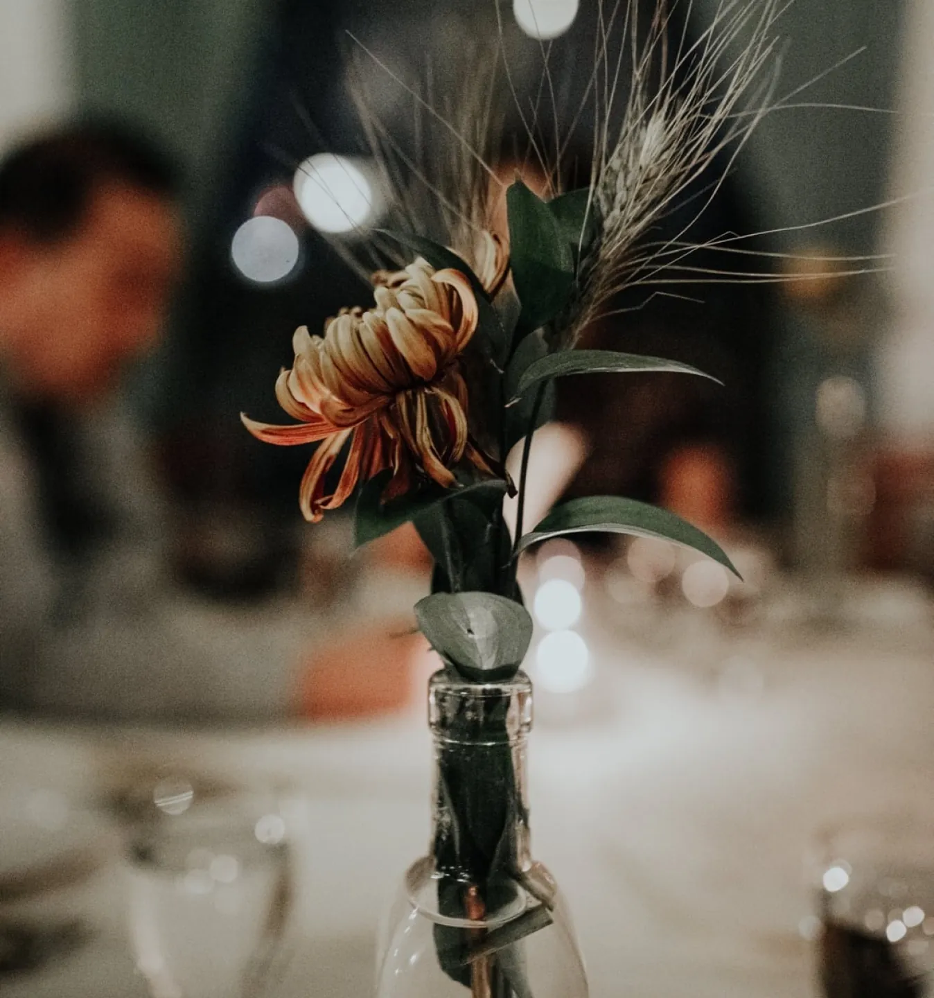 Dried floral arrangement in a glass bud vase on a restaurant table