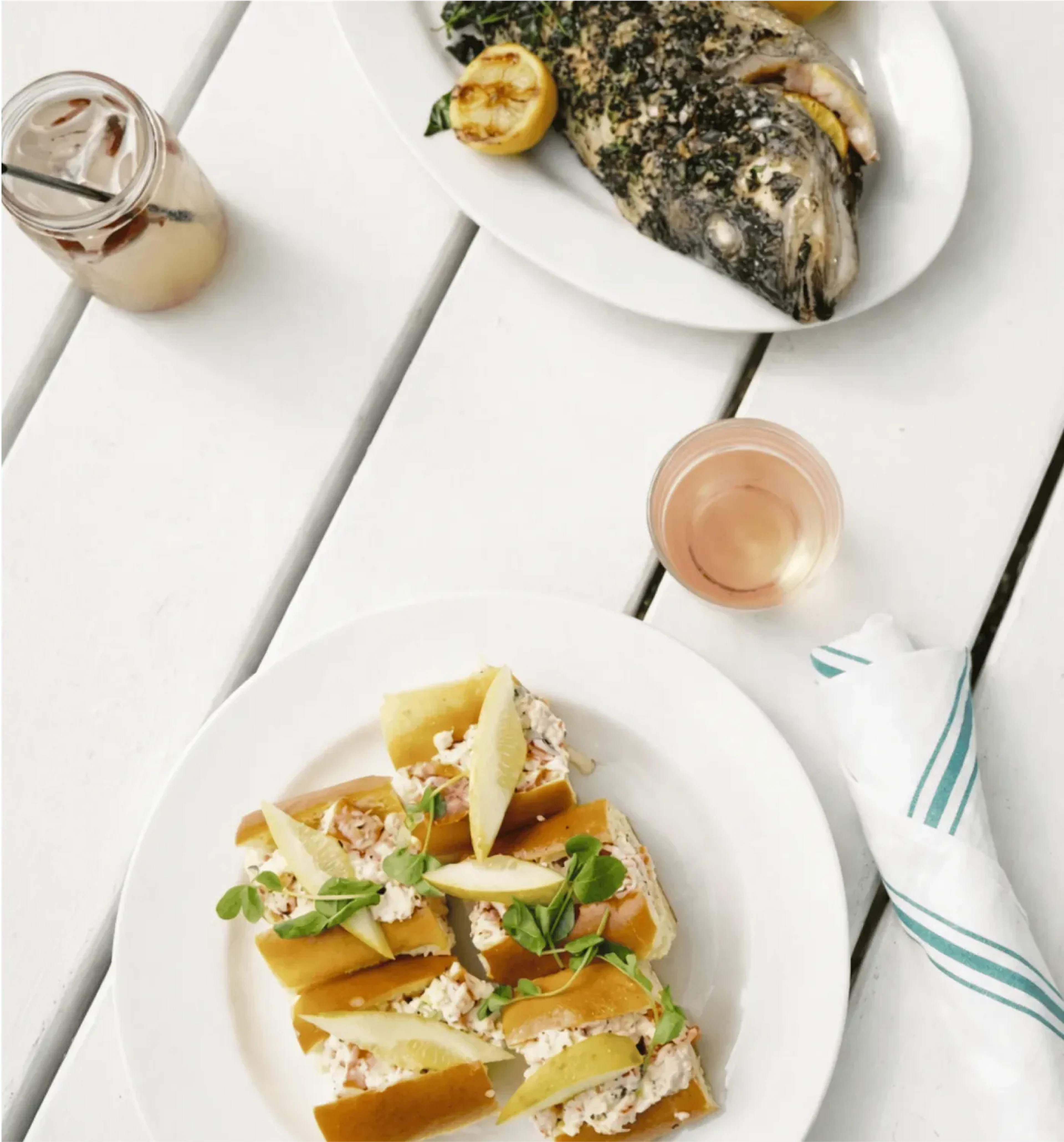Top-down photograph of meals on white plates that are sitting on white, wooden tables.