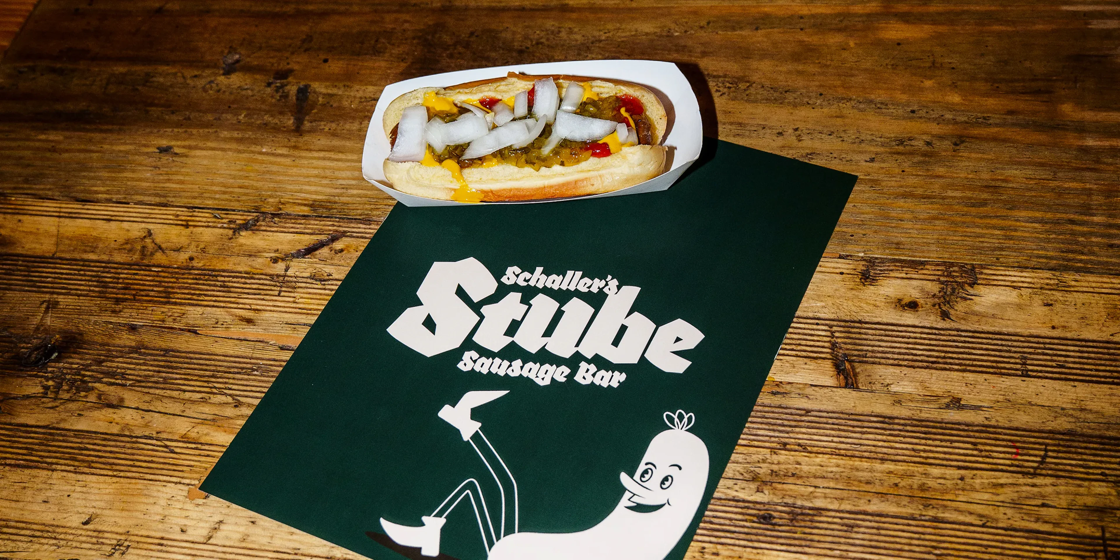Hot dog on a wood table beside a Schaller's Stube branded card