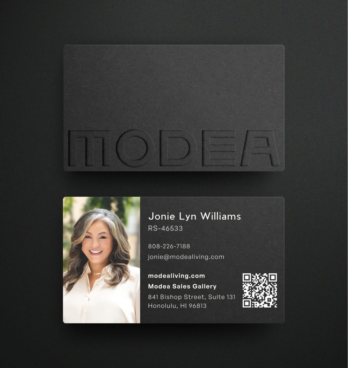 A matte black business card with a debossed Modea wordmark, resting on a dark surface, showing the sales agent's name, license number, and Sales Gallery address at 841 Bishop Street.