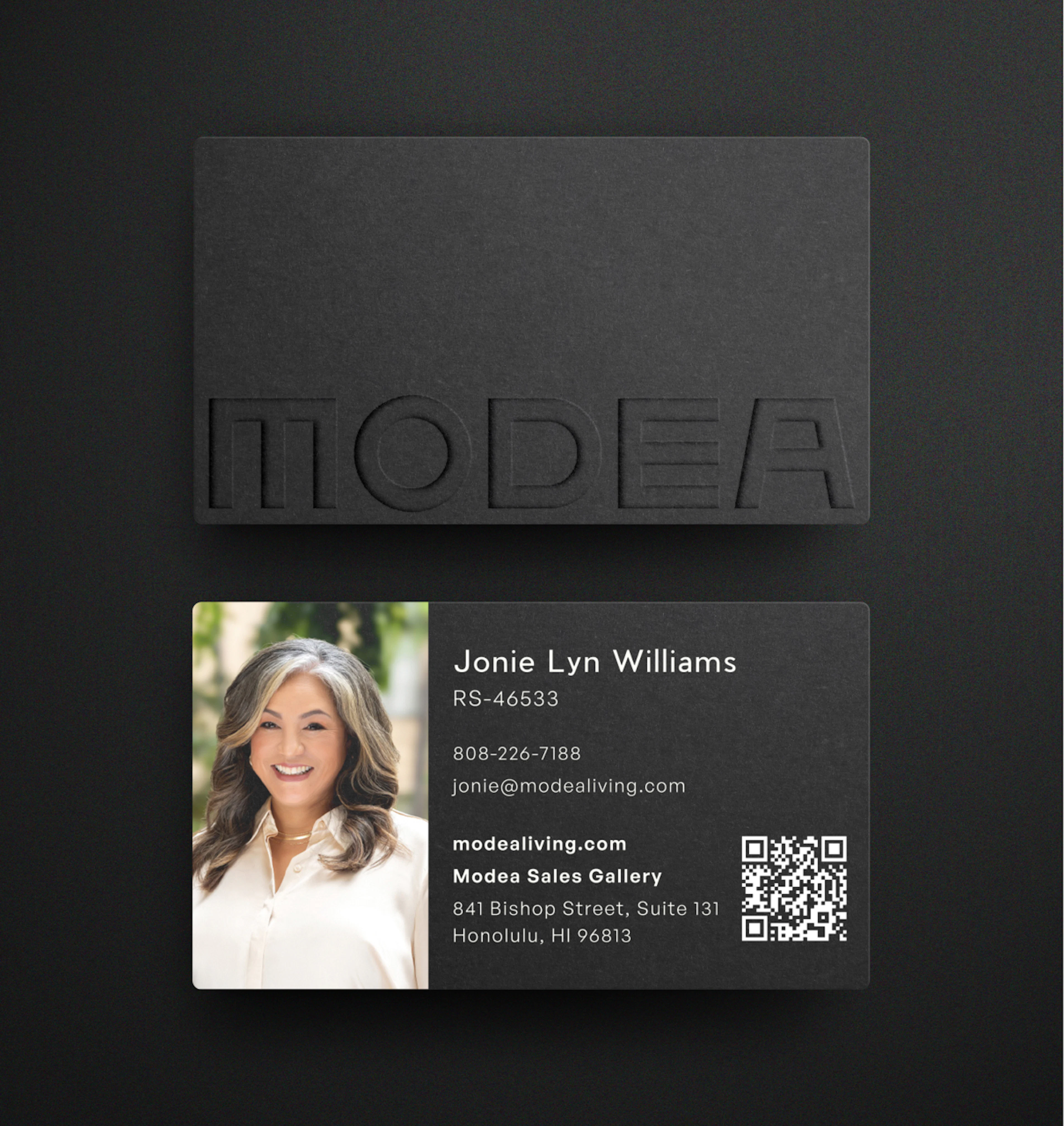 A matte black business card with a debossed Modea wordmark, resting on a dark surface, showing the sales agent's name, license number, and Sales Gallery address at 841 Bishop Street.