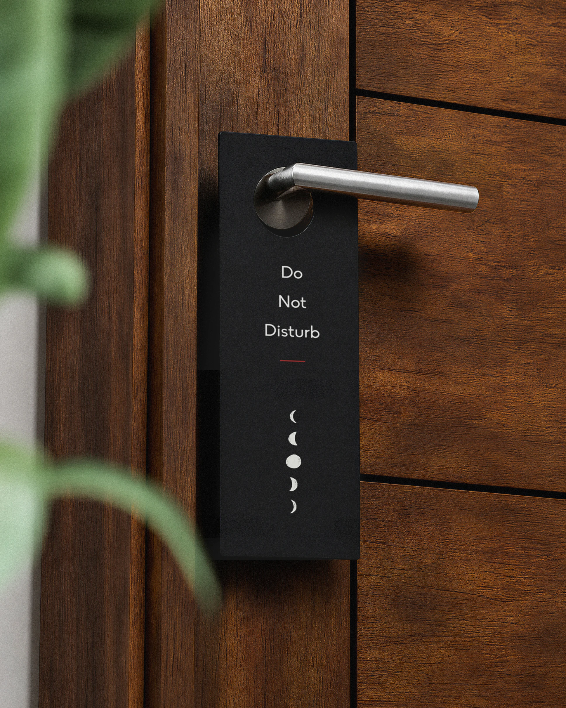 Black branded door hanger saying "Do not disturb" hanging on a silver door handle attached to a dark wood modern door