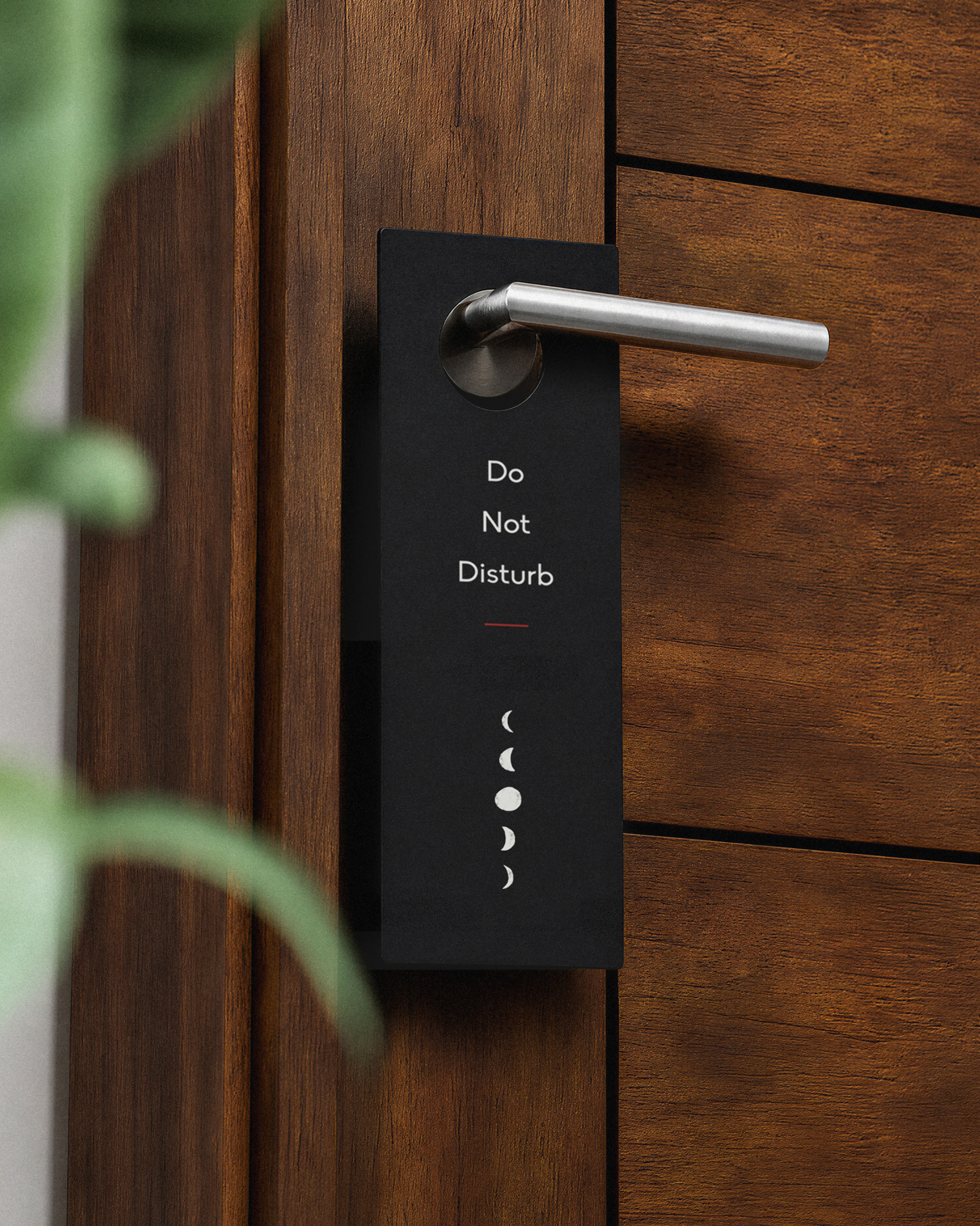 Black branded door hanger saying "Do not disturb" hanging on a silver door handle attached to a dark wood modern door