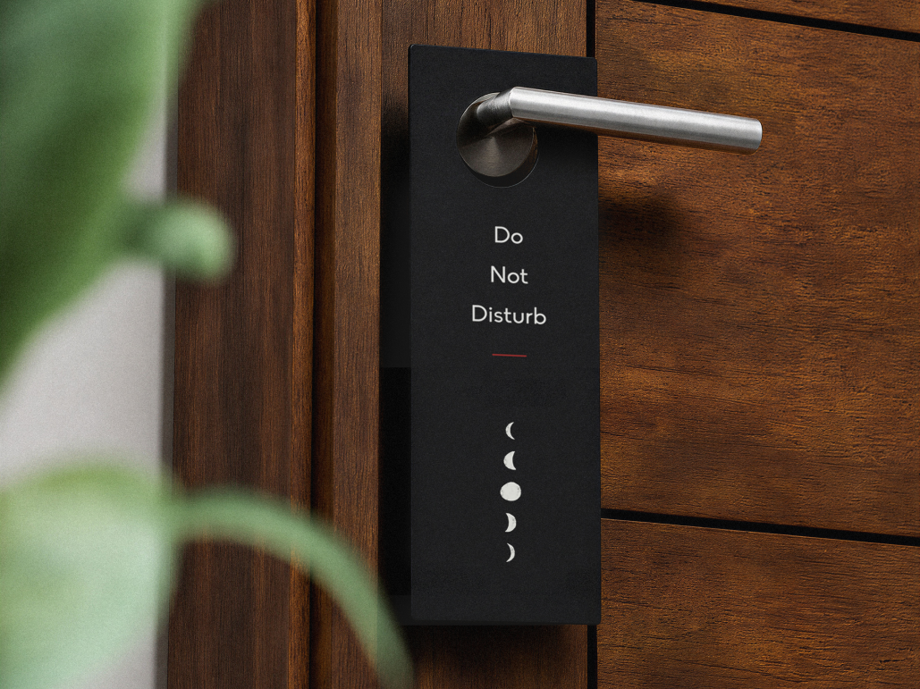 Black branded door hanger saying "Do not disturb" hanging on a silver door handle attached to a dark wood modern door