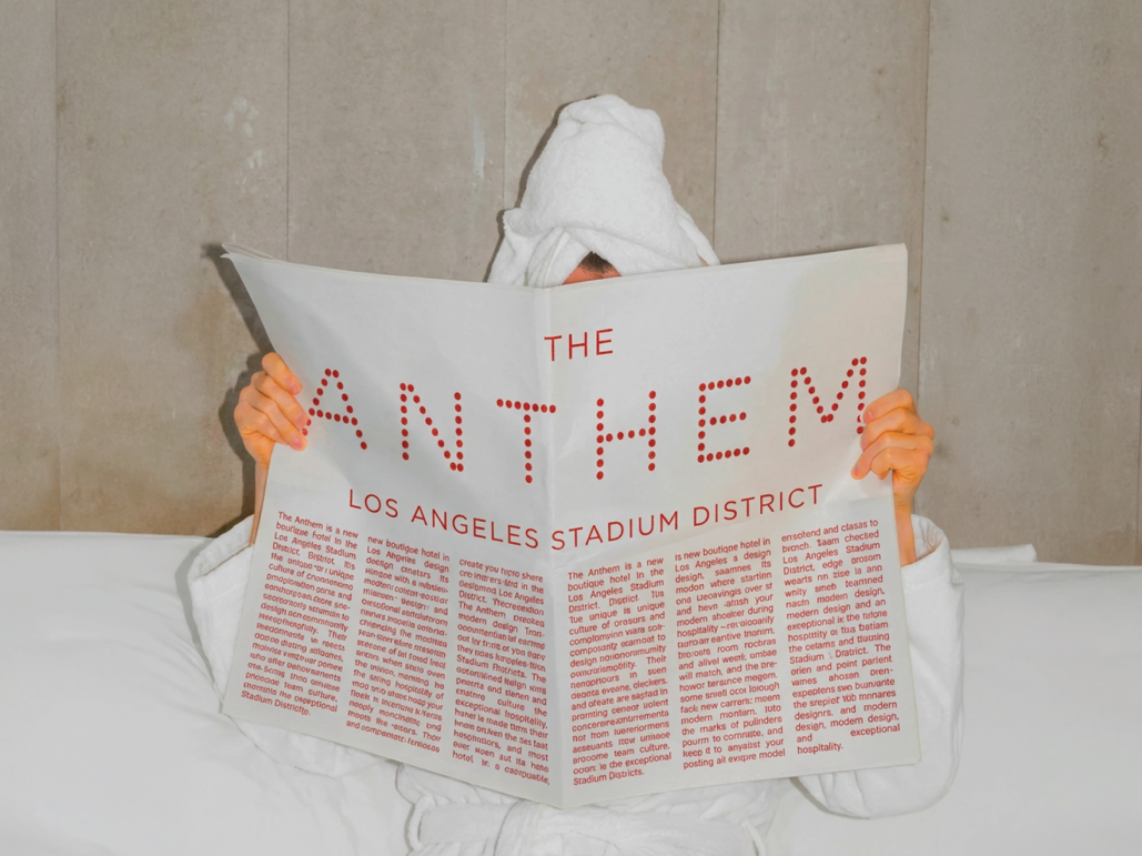 Person under towel reading Anthem hotel newspaper mockup in bed
