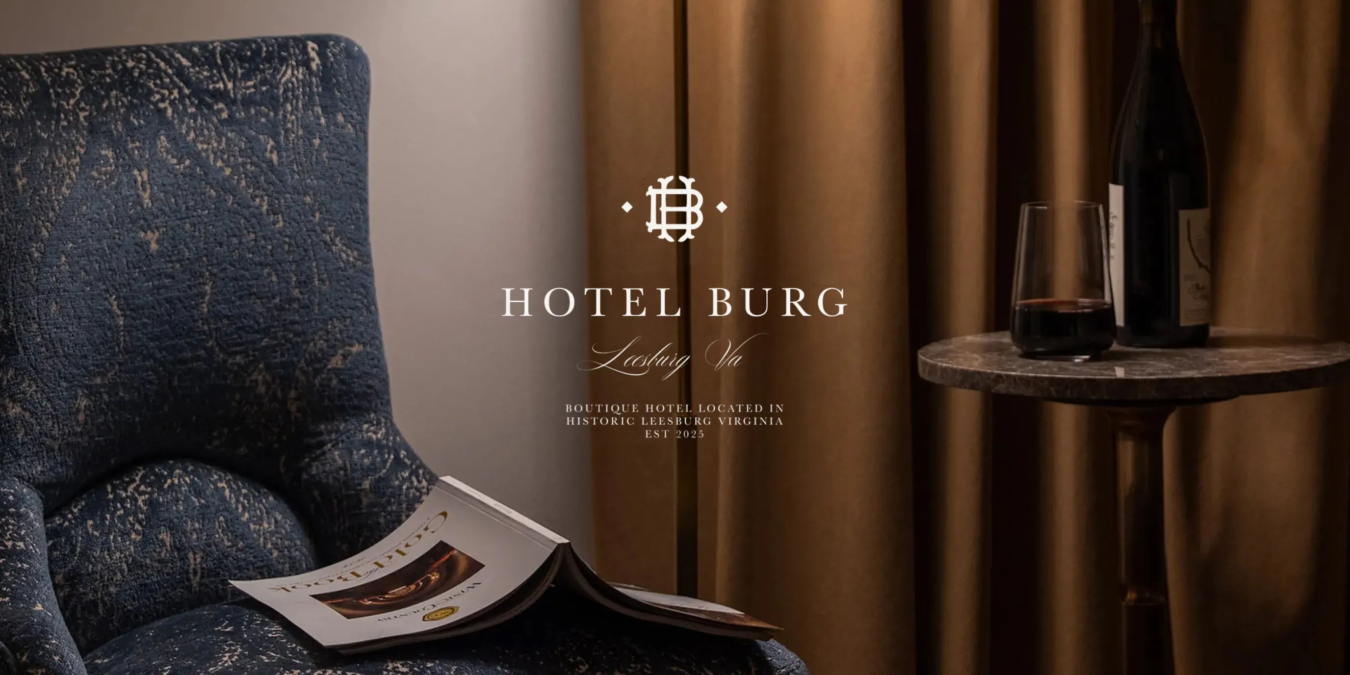 Hotel Burg logo over a blue upholstered armchair and wine glass on a side table