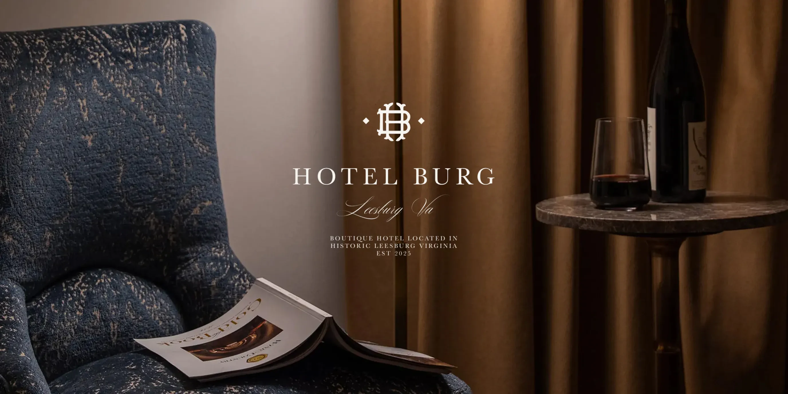 Hotel Burg logo over a blue upholstered armchair and wine glass on a side table