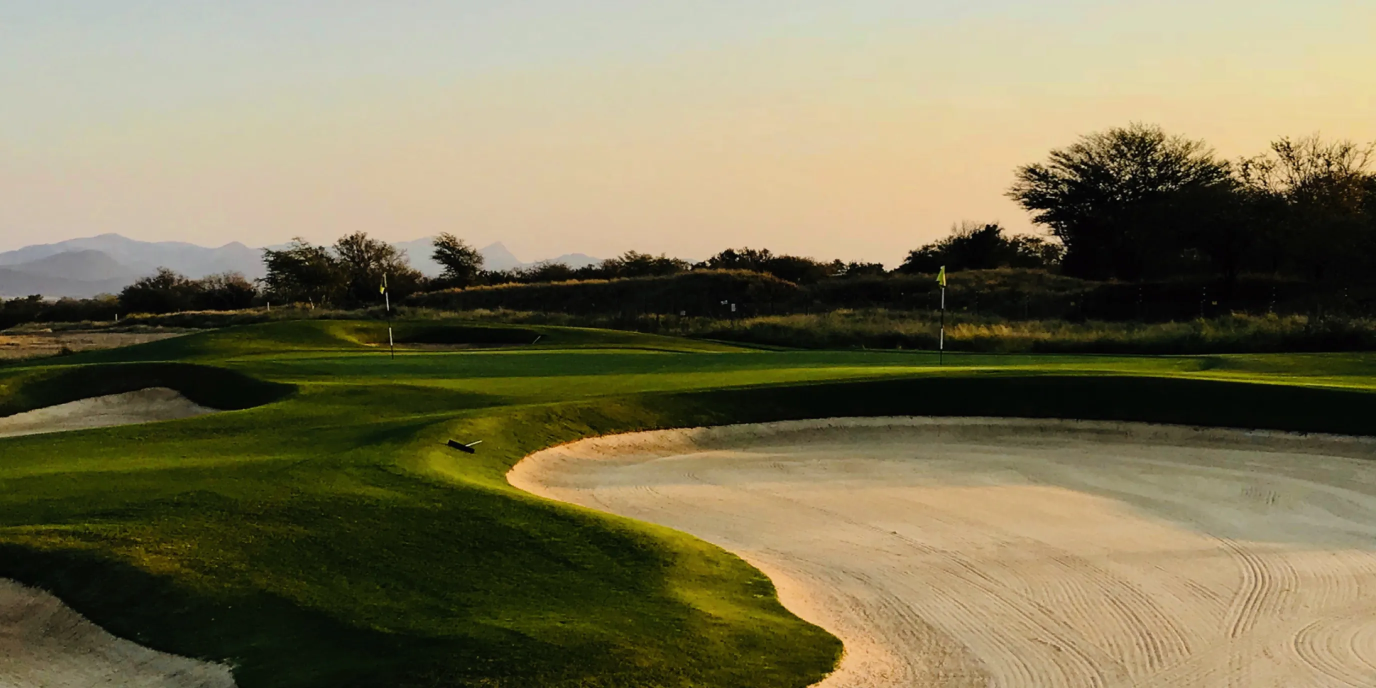 Golf course green and sand bunker at sunset with mountains in the distance